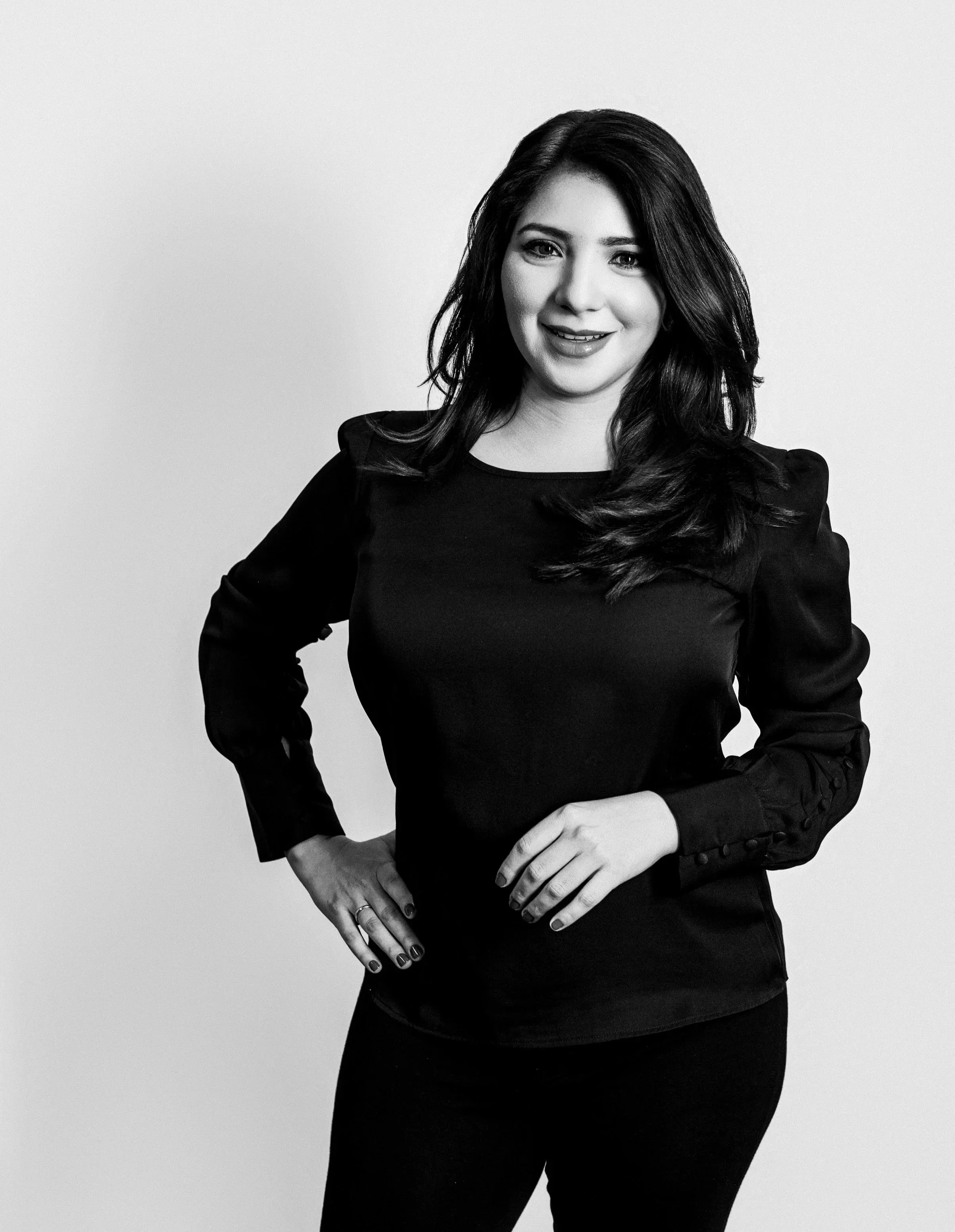 Retrato en blanco y negro de una mujer sonriente con blusa negra y la mano en la cintura