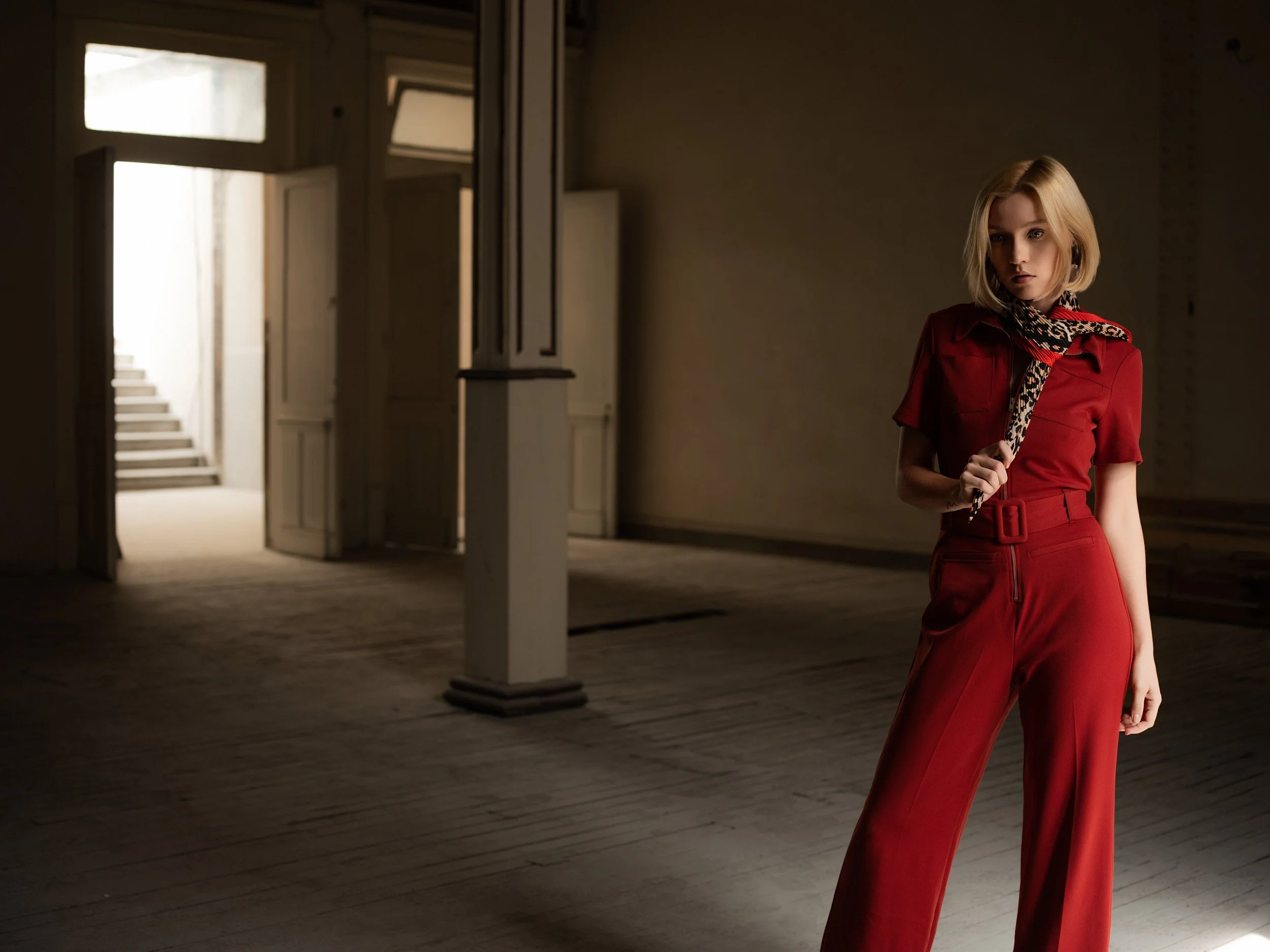 Retrato de una mujer con overol rojo junto a una columna en un edificio antiguo