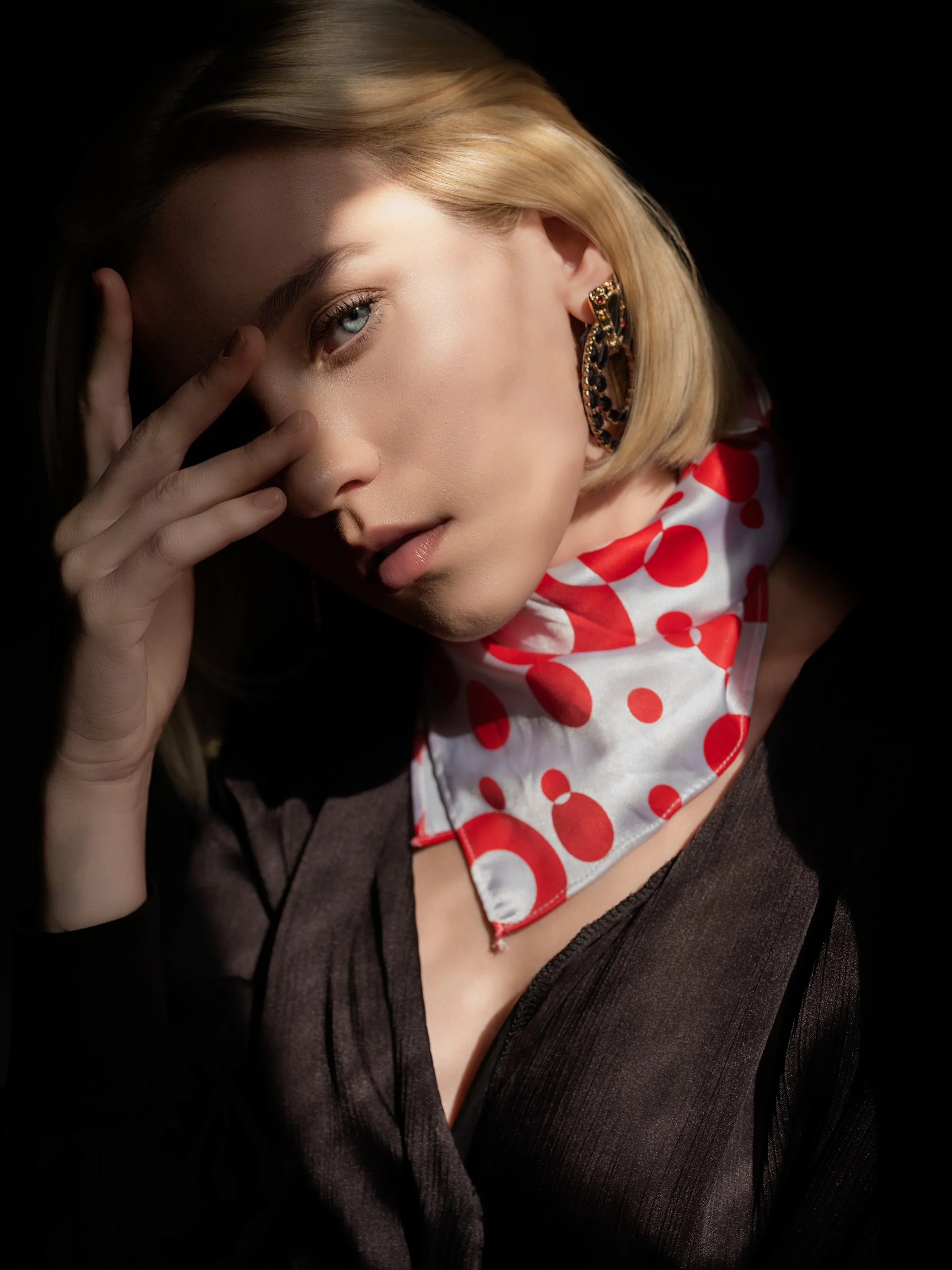 Editorial fashion portrait of a woman wearing a red patterned scarf, photographed in studio with controlled lighting.