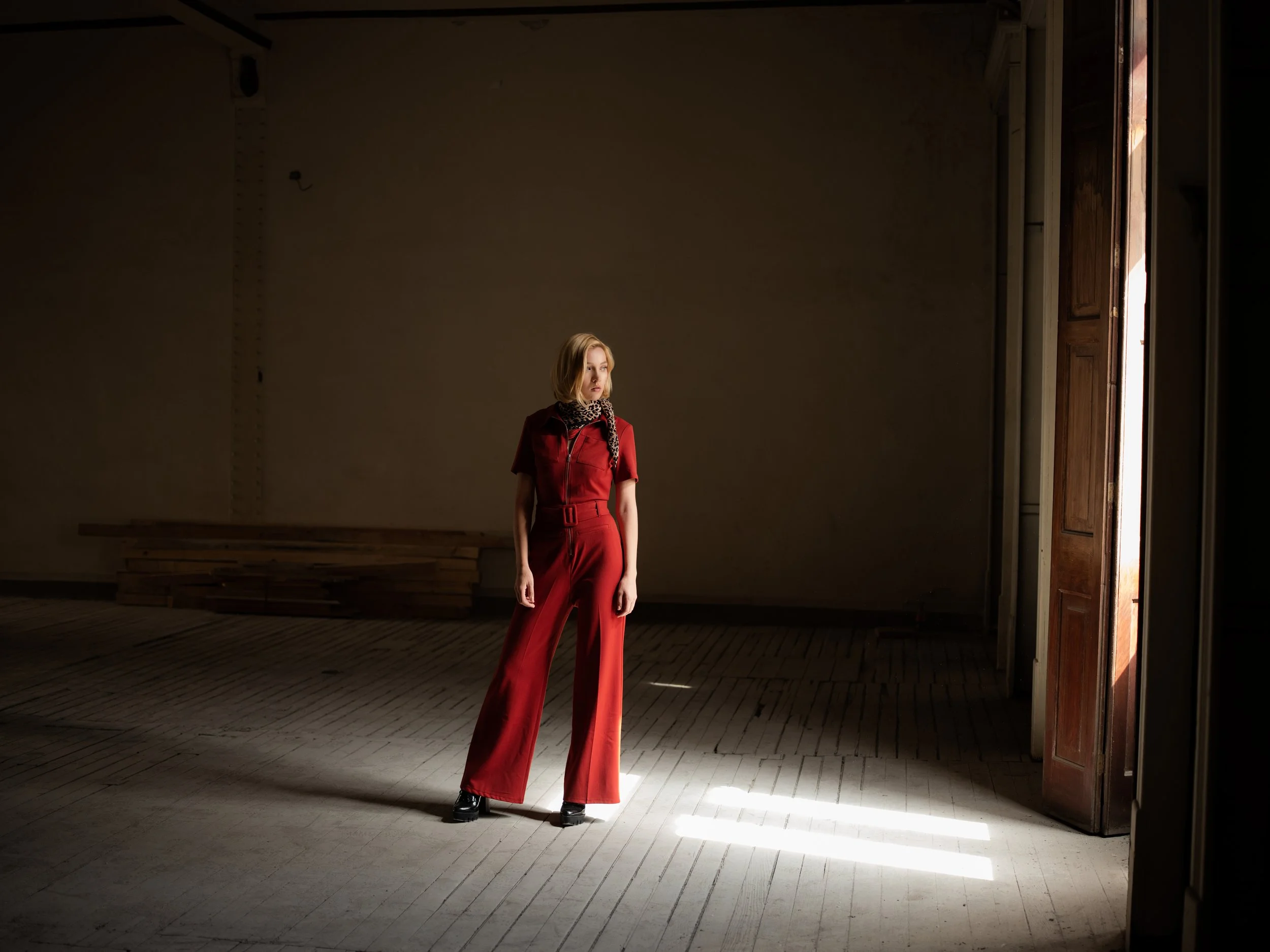 Retrato de una mujer con overol rojo en un salón vacío con luz de ventana