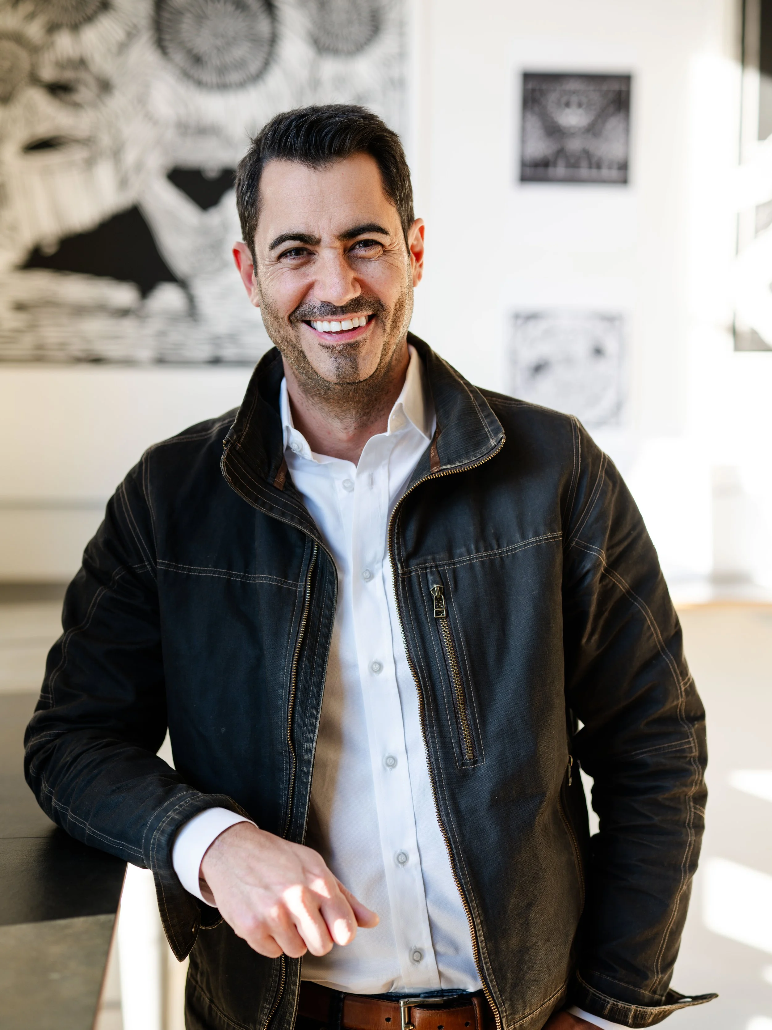 Daria wearing a dark denim jacket and white shirt, smiling, right arm leaning on a counter