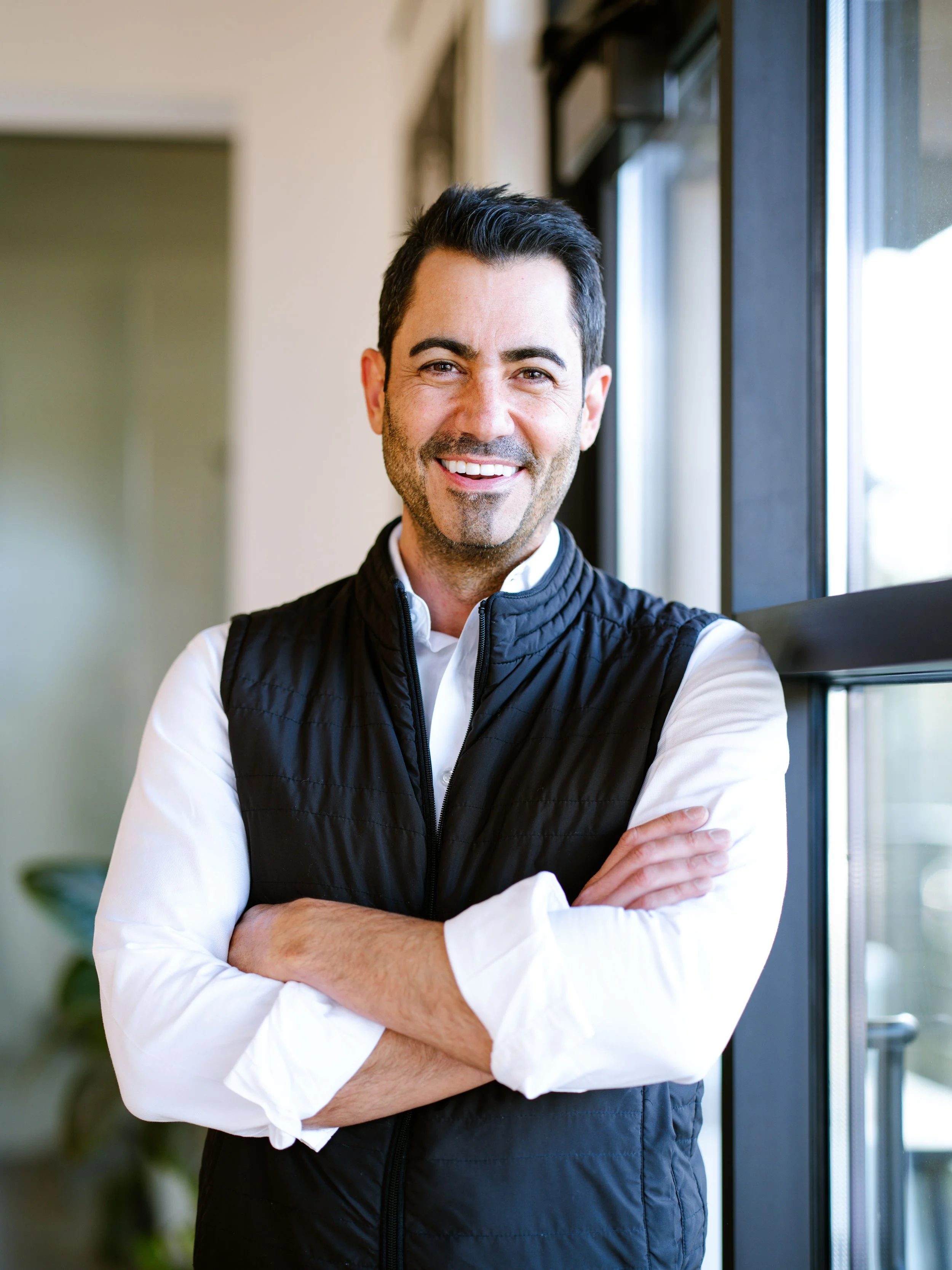 Headshot of Daria smiling with arms crossed,  wearing white shirt and black vest