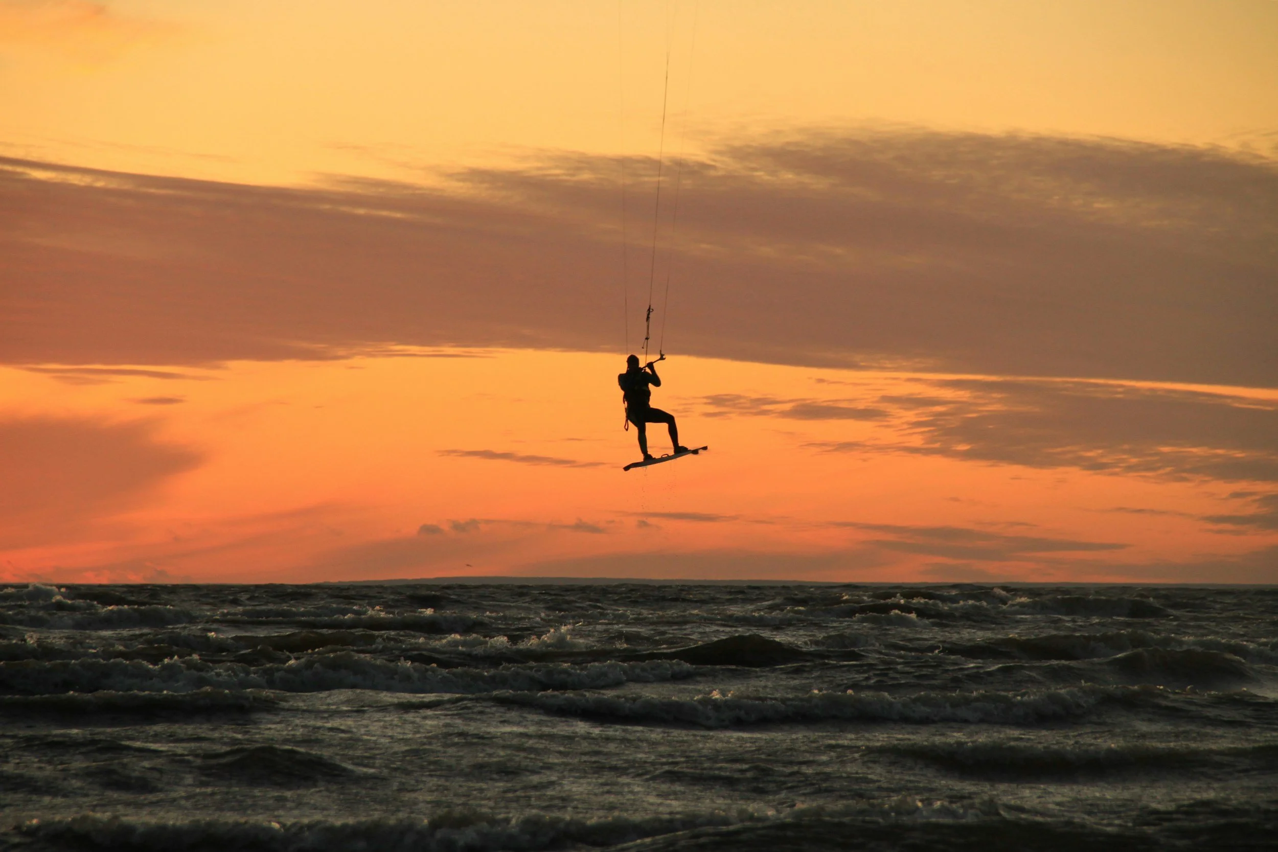 Person kiteboarding on the ocean at sunset