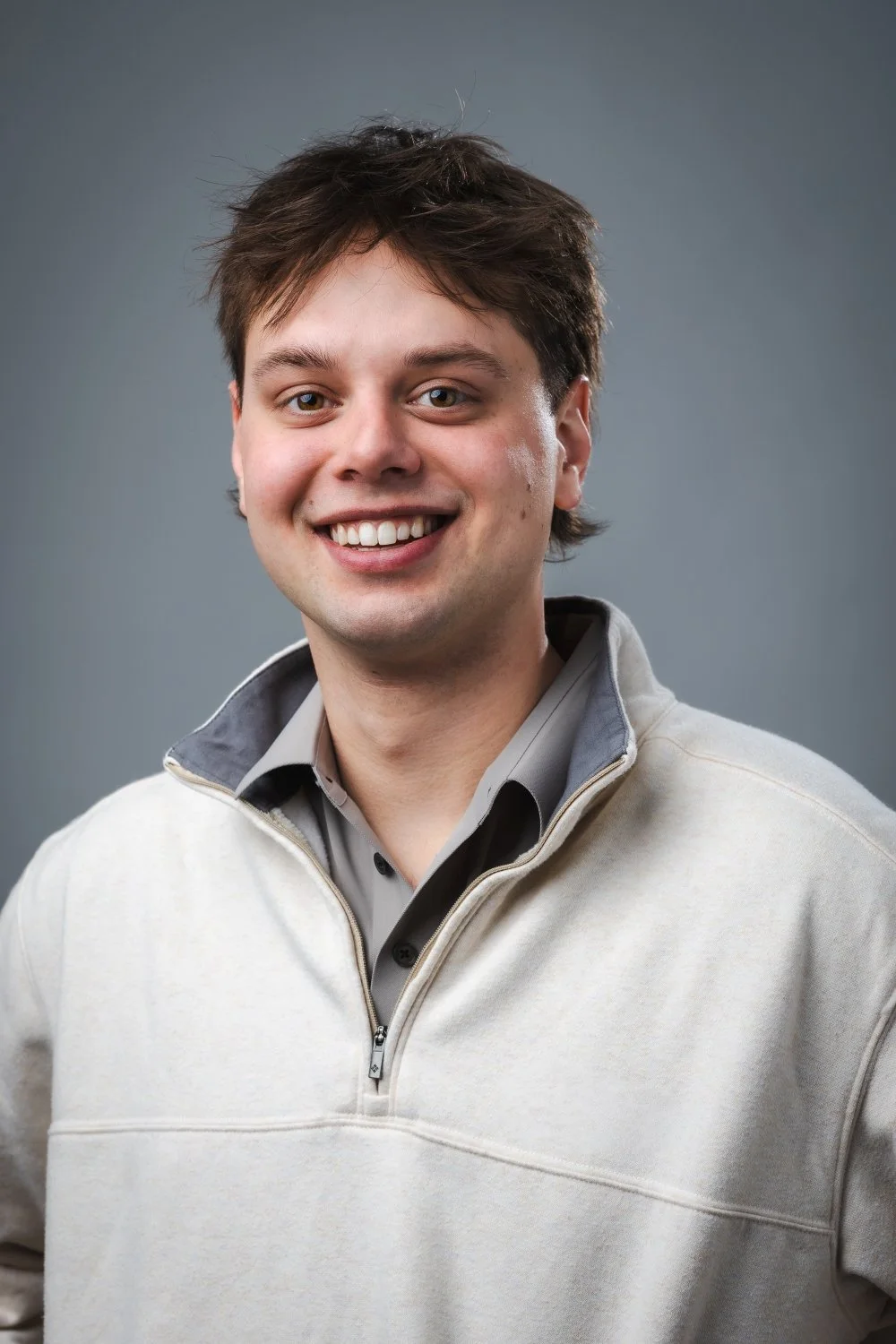 Senior portrait of a young man smiling wearing against a gray background in a studio