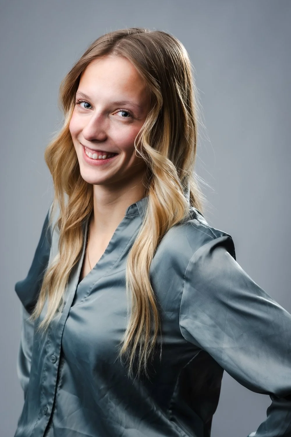 Senior portrait of a young woman smiling wearing nice clothes against a plain gray background in a studio