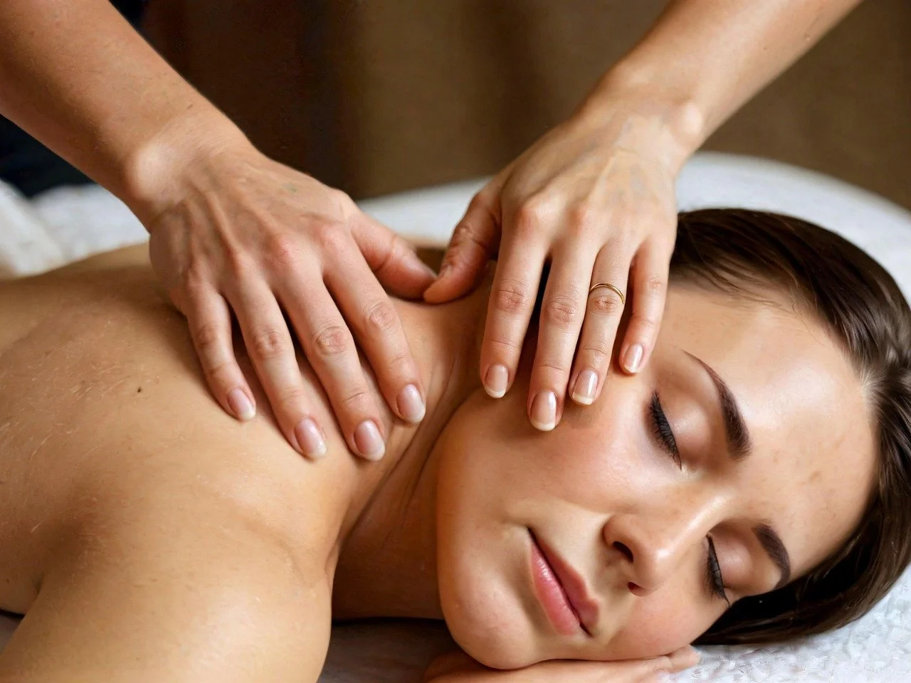 A woman receiving a massage on her shoulder from a massage therapist in a spa setting.