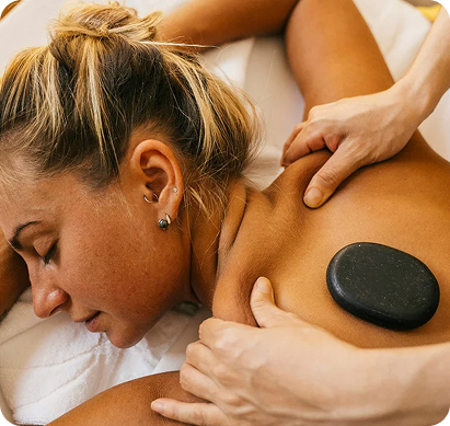 A woman receiving a massage with a hot stone placed on her shoulder.