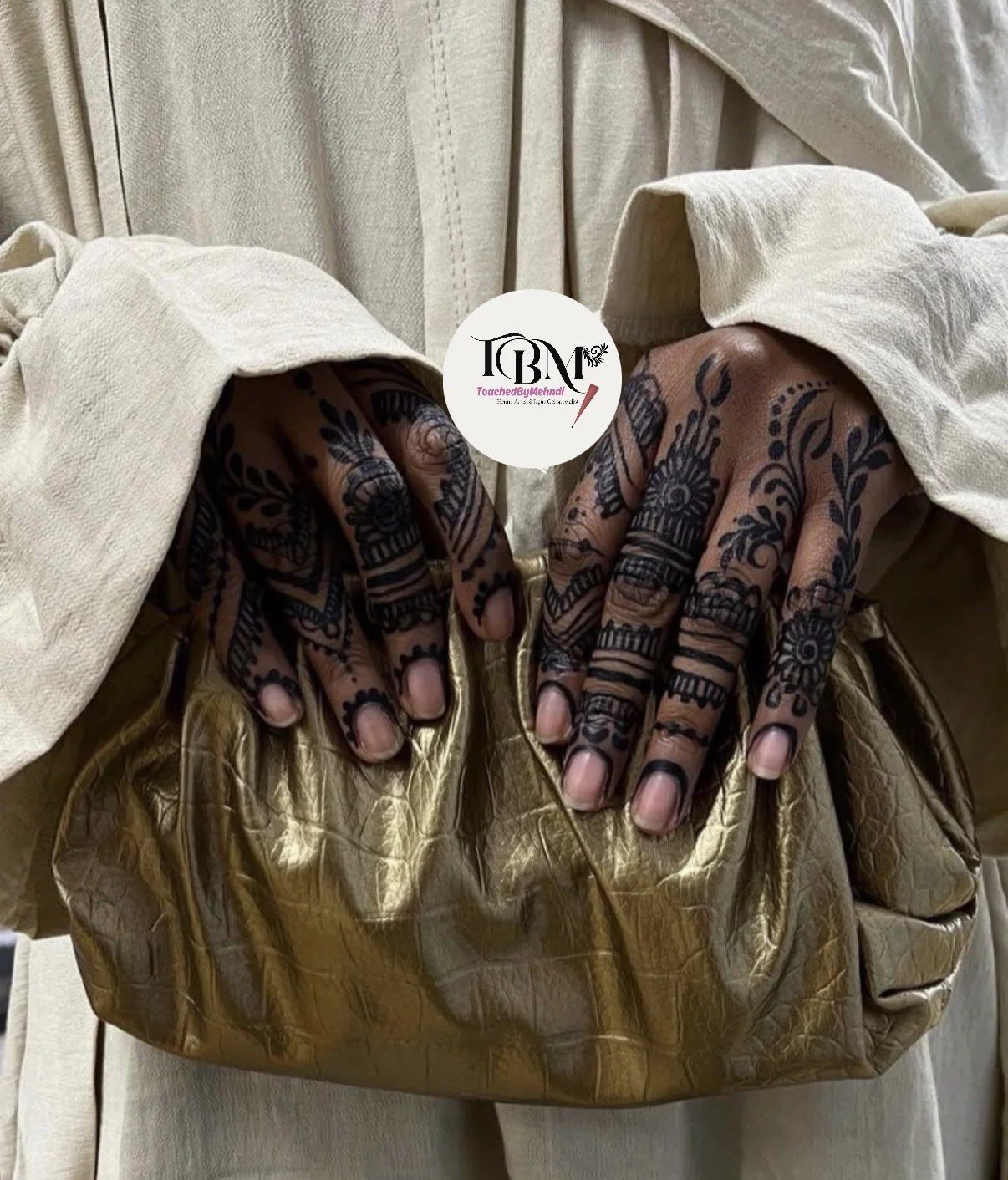 Hands with intricate henna designs resting on a gold purse, wearing a beige or cream-colored outfit.