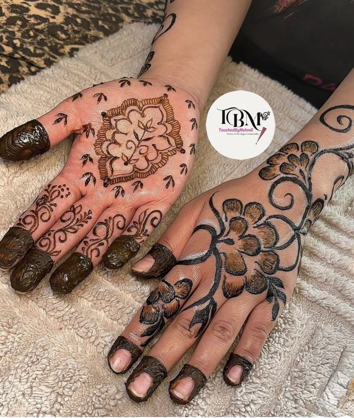 Two hands with intricate hennas and black nail polish with digital wedding details logo in the middle.