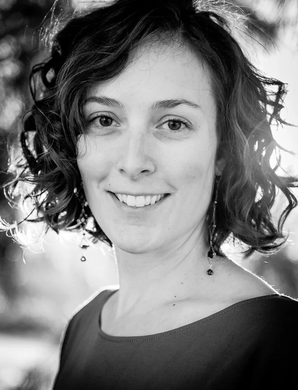 Black and white portrait of a woman with curly hair, smiling, outdoors with blurred background