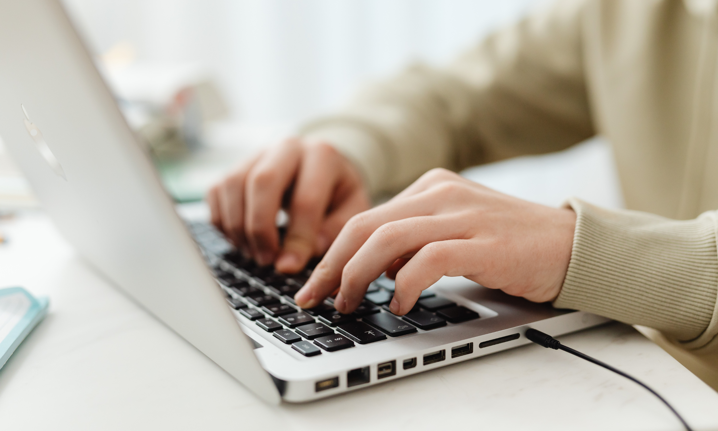 Person typing on a laptop keyboard with a beige long sleeve shirt.