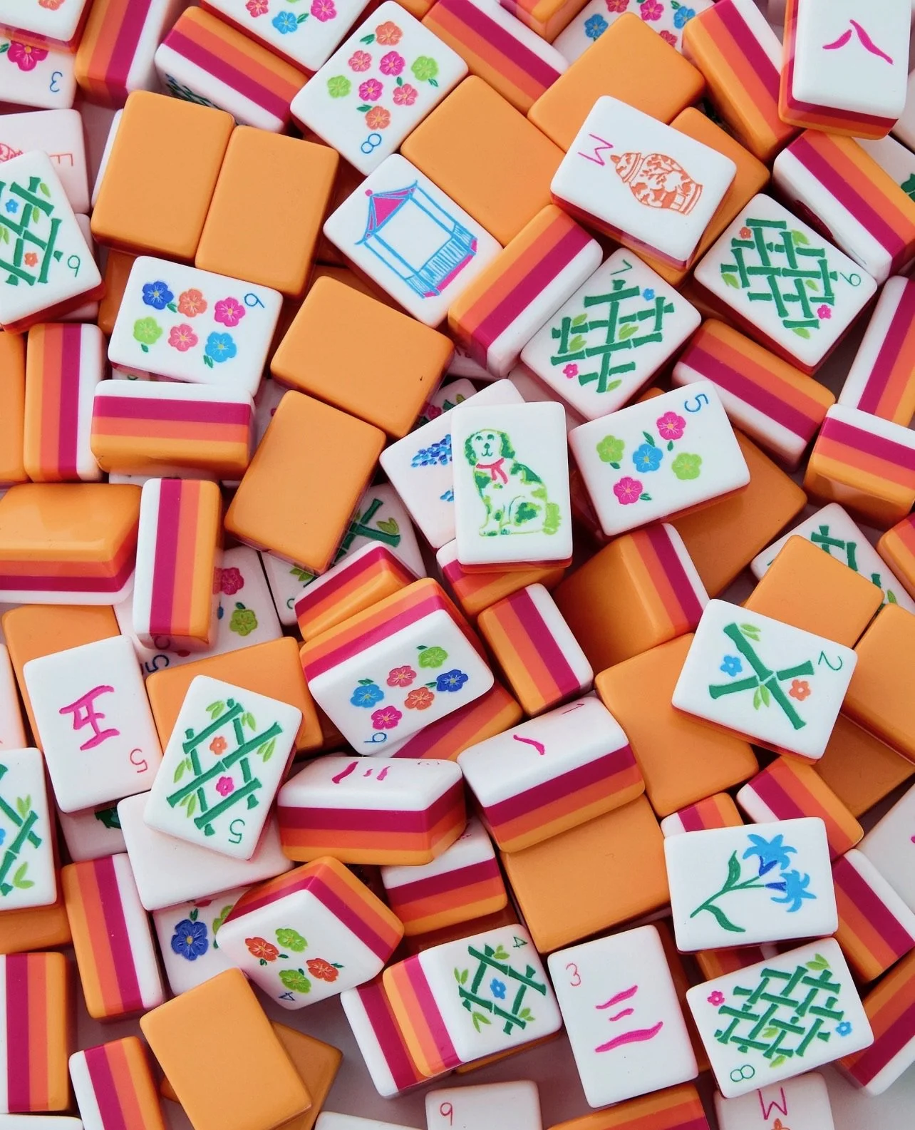 A collection of colorful Mahjong tiles with floral, geometric, and subject patterns, some orange solid tiles, and some tiles with pink and orange striped pattern.