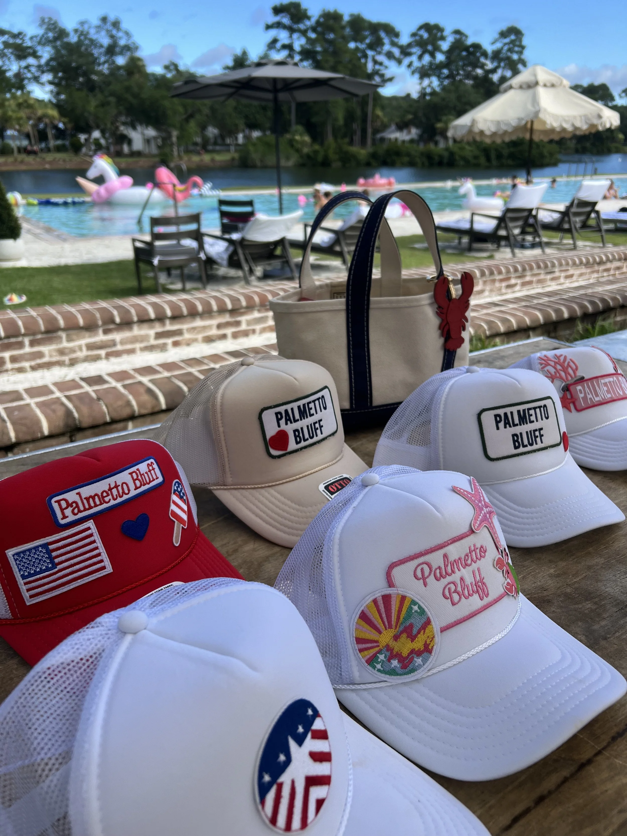 A collection of white and red baseball caps with patches and embroidery, featuring designs such as flags, stars, and landmarks, arranged on a wooden surface.