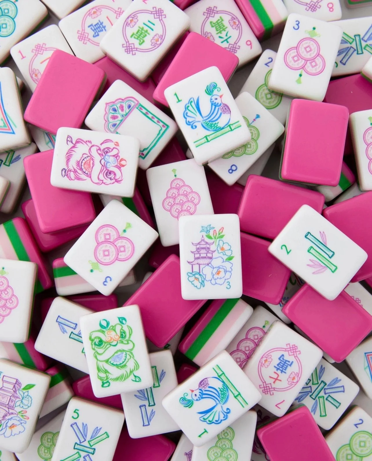 A pile of colorful mahjong tiles, mostly white and pink, with various traditional Chinese symbols and designs, including animals, flowers, and pagodas.