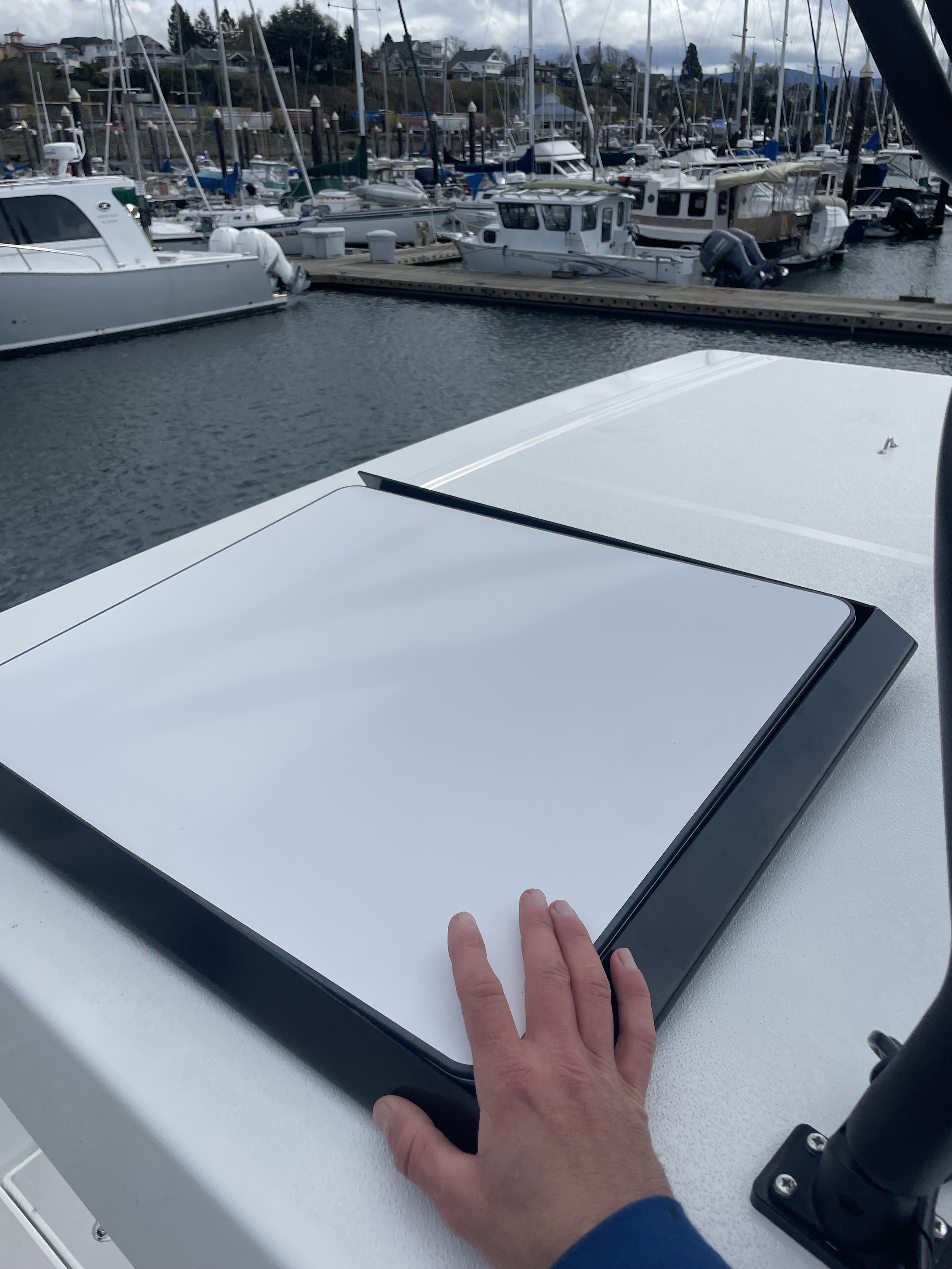 A person's hand on a white surface with boat docks and numerous boats in the background.