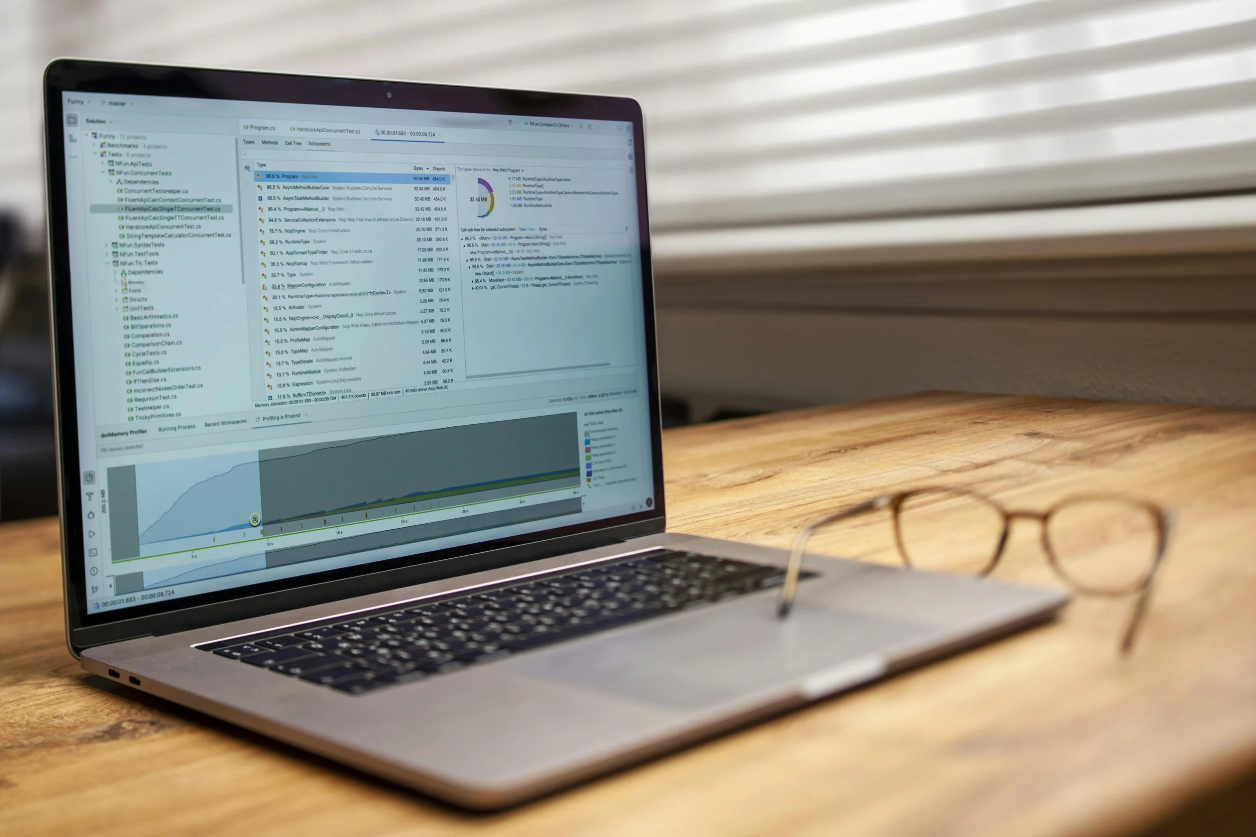A laptop on a wooden desk displaying a resume or CV on its screen, with glasses beside it.