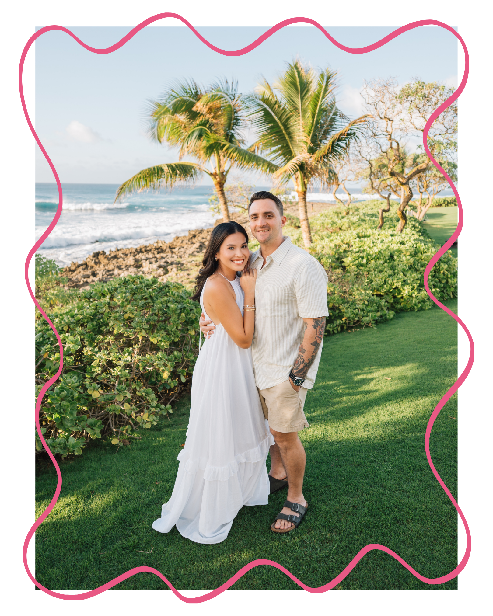 A happy couple standing outdoors near the beach with palm trees and greenery in the background, smiling at the camera.