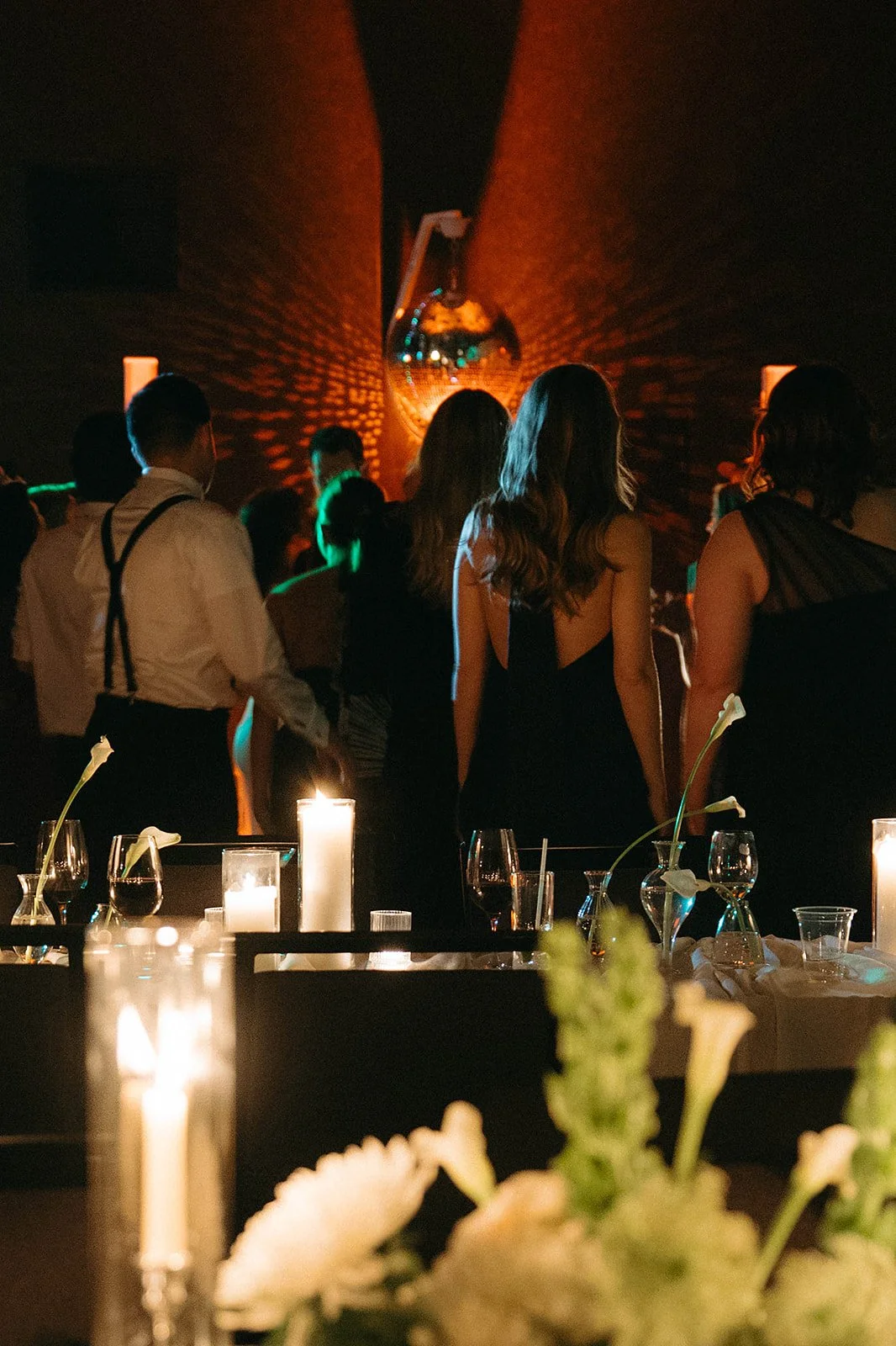 People dancing at a dimly lit party or event with candles on tables and a disco ball reflecting light on the walls.