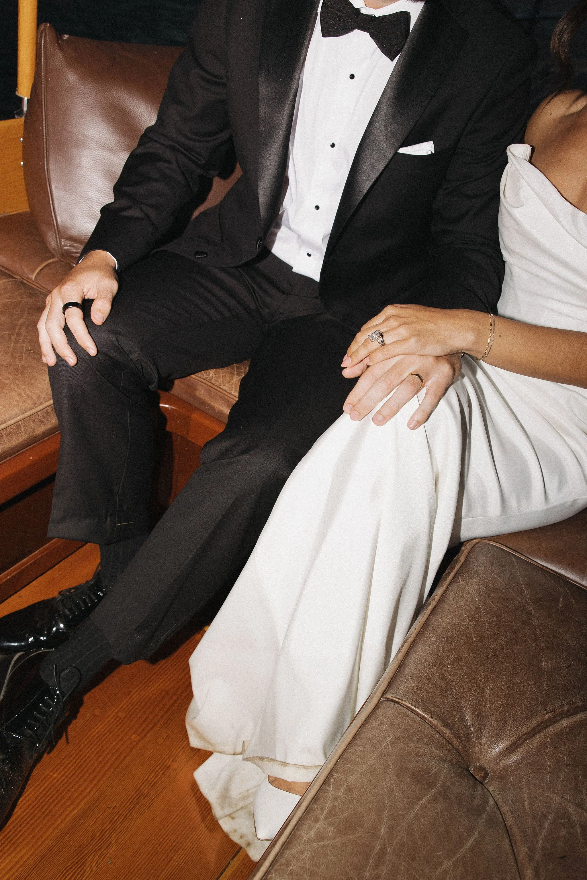 Close-up of a wedding couple sitting together, dressed in formal attire; the groom in a black tuxedo and the bride in a white wedding dress.