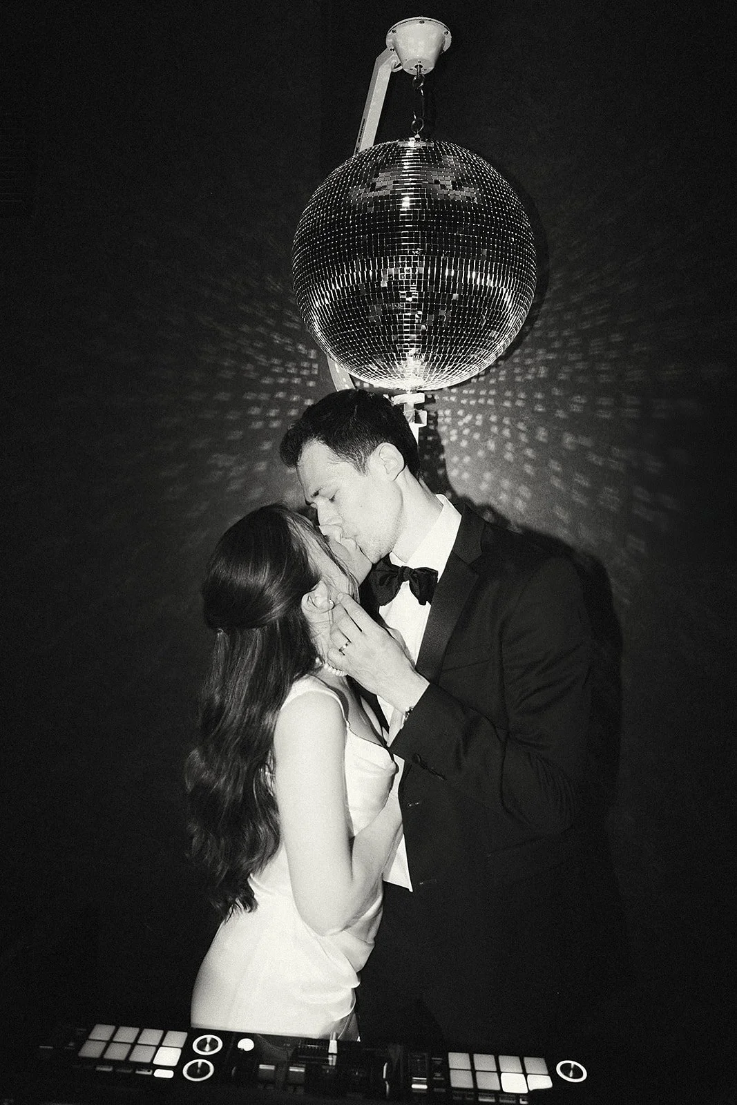 A couple in formal attire kissing under a disco ball at a party or event.