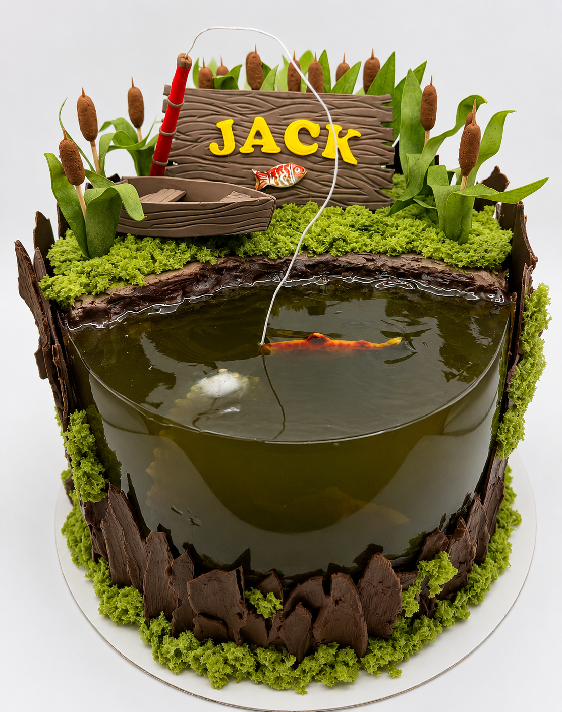 A creative fishing-themed birthday cake featuring a realistic edible pond with koi fish details, rustic wood textures, cattails, moss accents, and a miniature rowboat scene. Personalized with a custom name sign and fishing rod detail, this unique cak