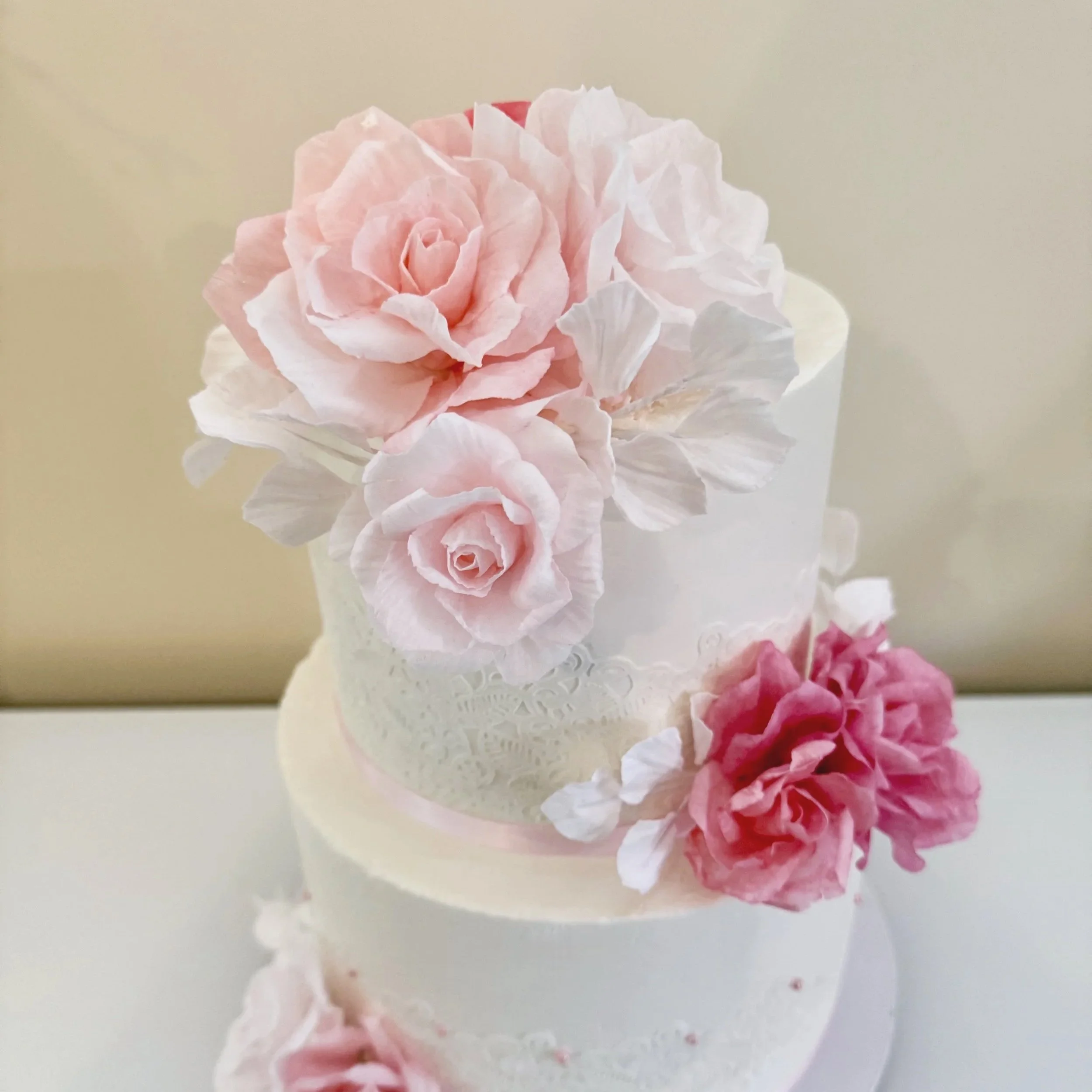 Two-tier white wedding cake decorated with pink and white sugar flowers, topped with large pink roses.