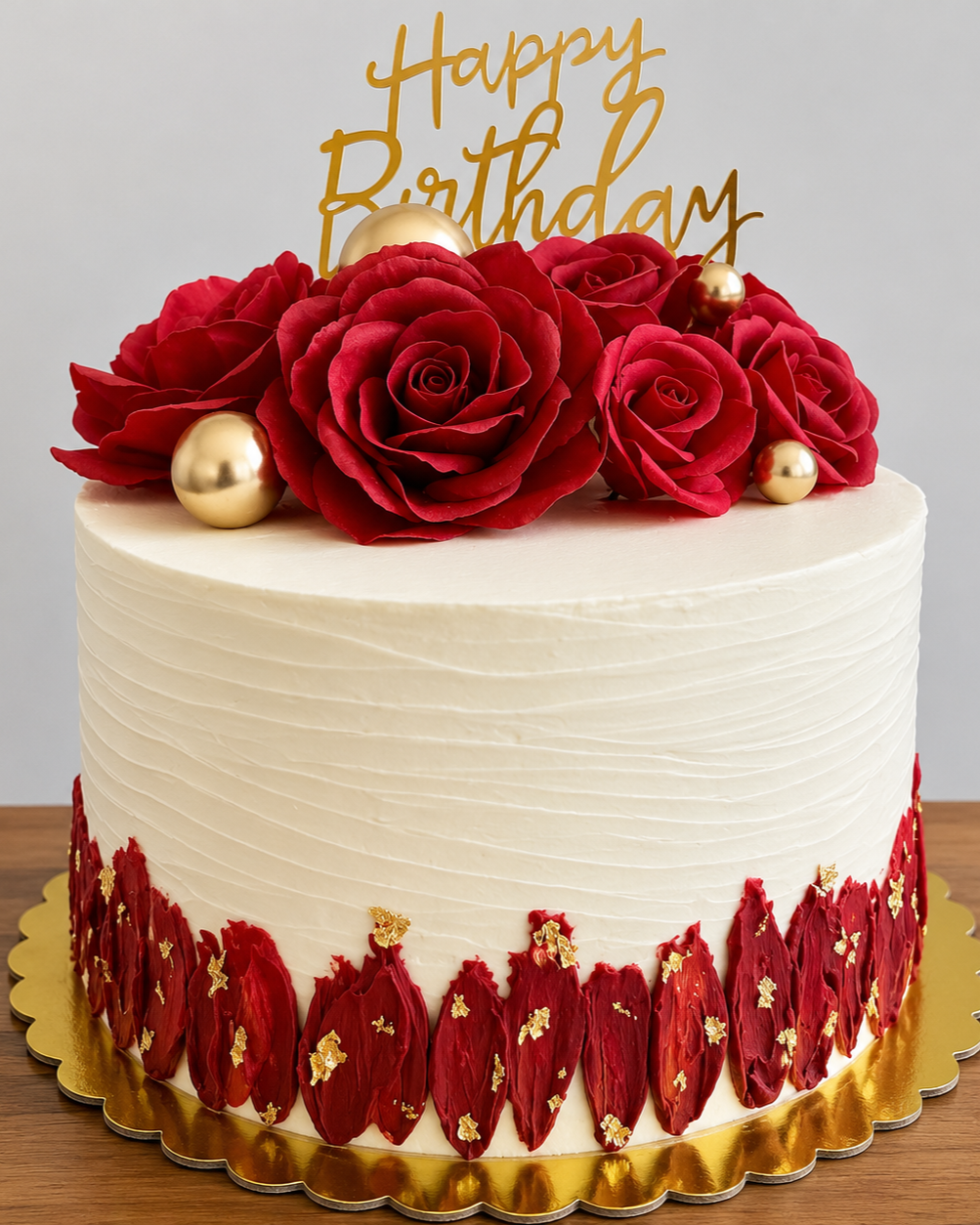 A birthday cake decorated with handcrafted wafer paper red roses, gold leaf, and topped with a gold 'Happy Birthday' topper.