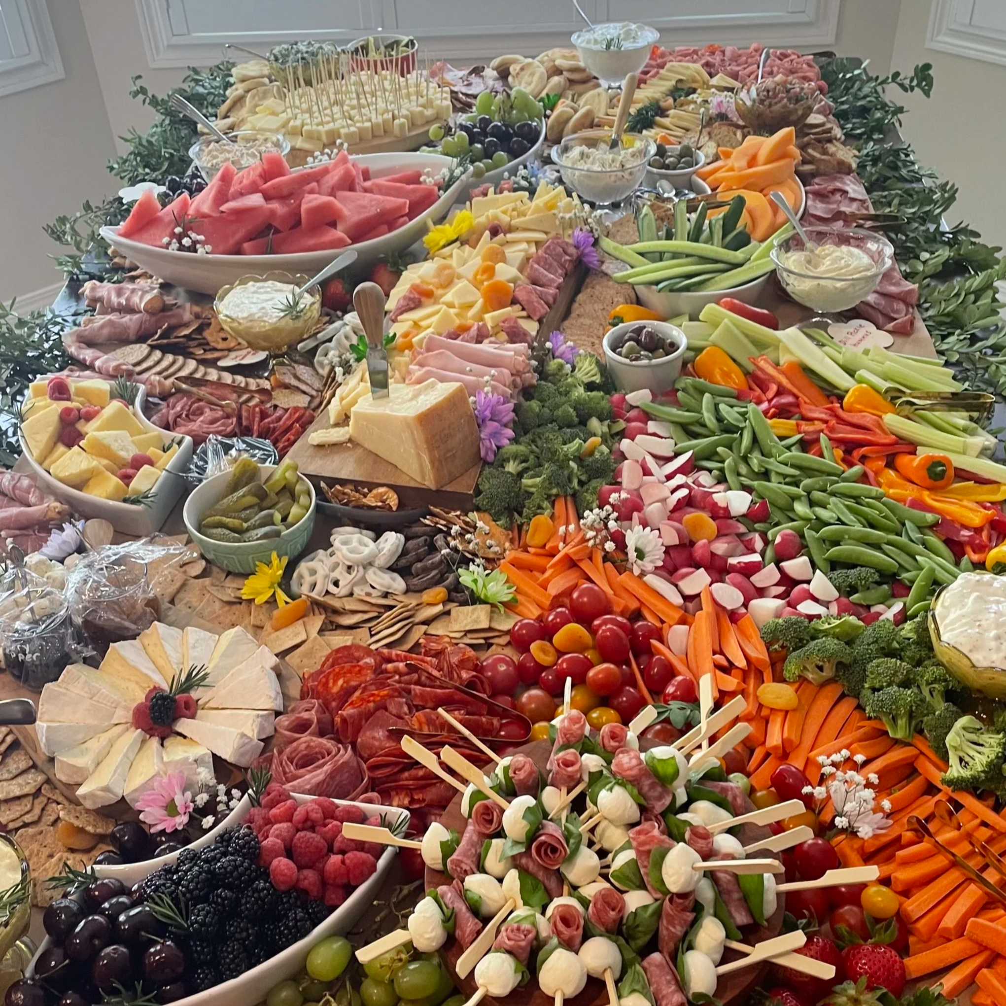 A large table filled with various colorful fruits, vegetables, cheeses, meats, and snacks, arranged for a buffet or party. Grazing table in Calgary by Graze & Glaze’d