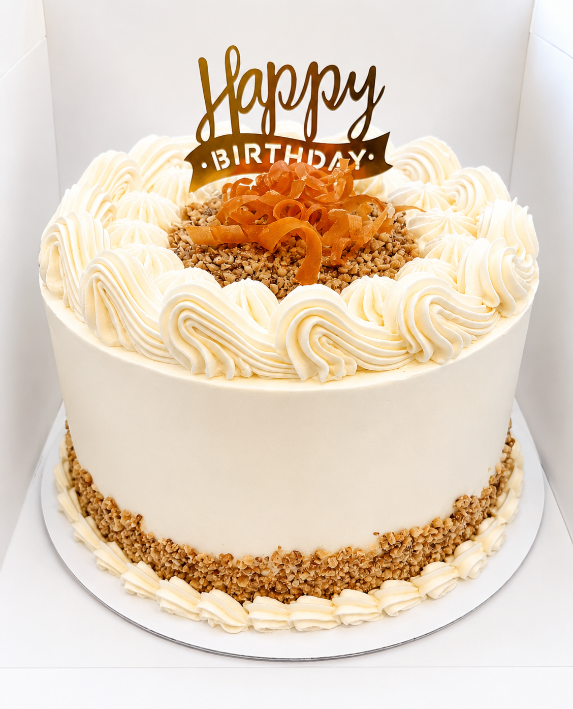 A timeless carrot cake finished with smooth cream cheese frosting, elegant vintage piping, and a crunchy walnut crumble border. Topped with delicate candied carrot ribbons and a gold “Happy Birthday” topper, this classic dessert combines rustic charm