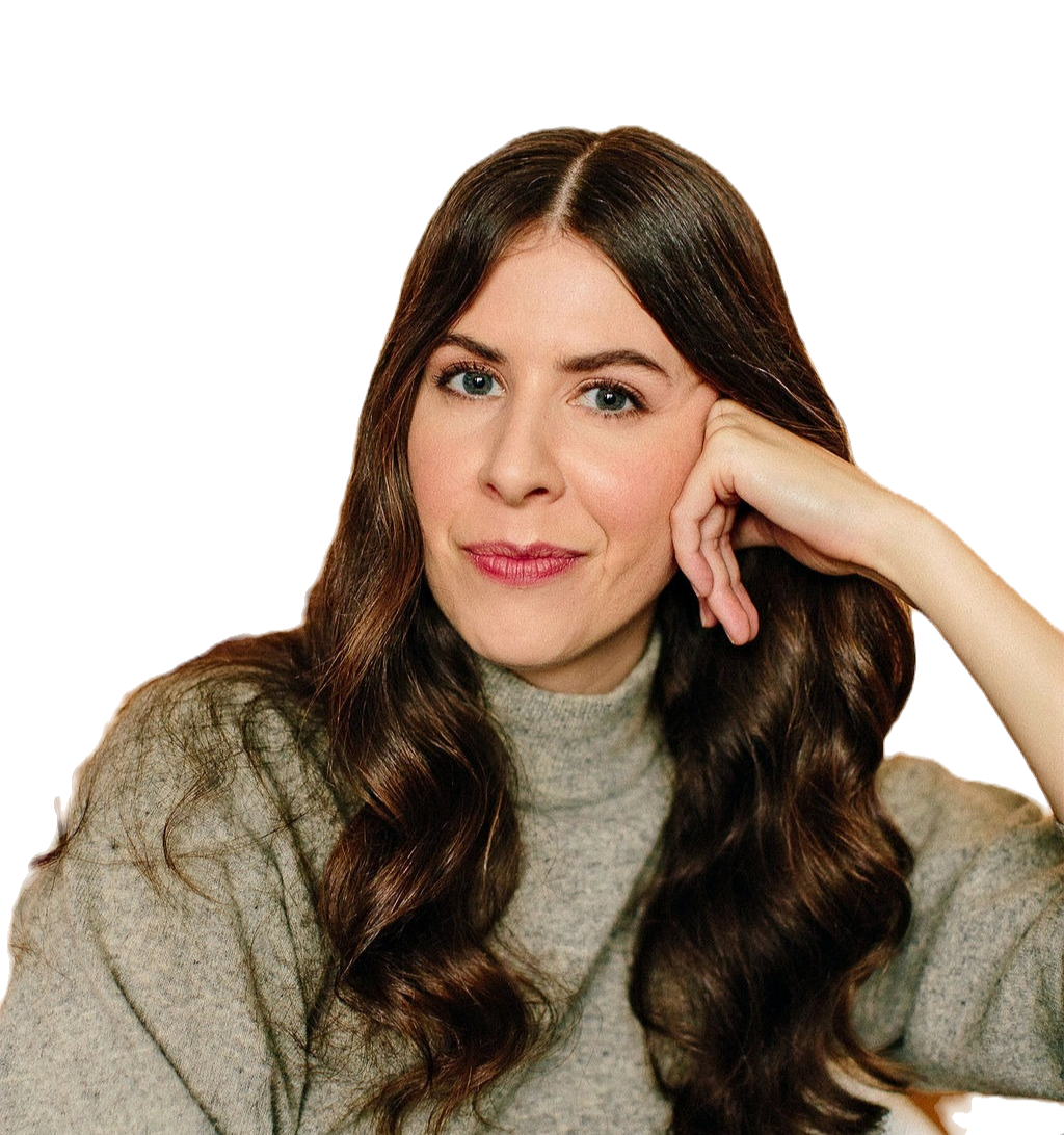 A young woman with long brown hair, wearing a beige sweater, is sitting with her head resting on her left hand, looking directly at the camera with a slight smile.