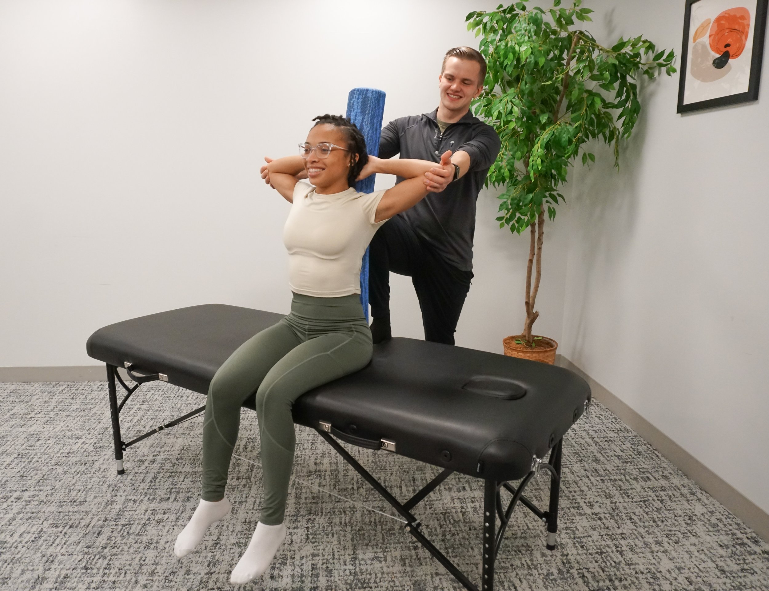 Woman receiving assisted back stretch using a foam roller in a wellness studio.