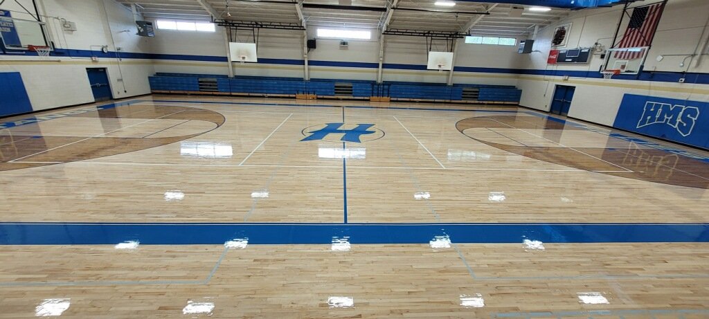 Empty indoor basketball court with blue and white color scheme and the initials 'HMS' painted at the center.