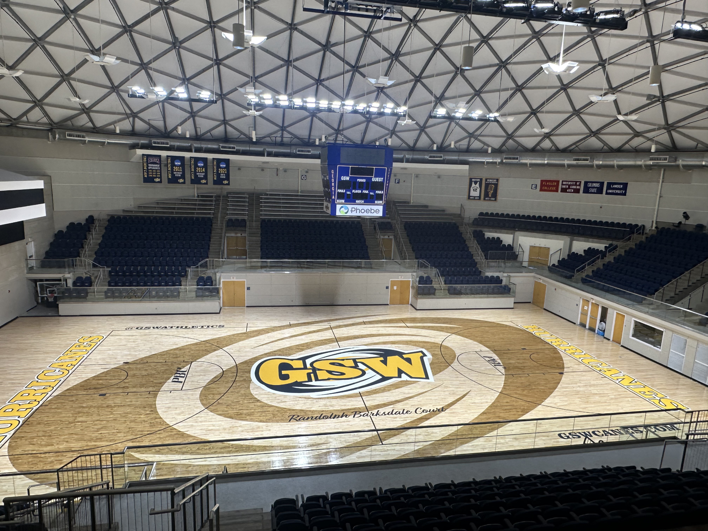 Empty basketball court with GSW logo in the center and seating on all sides inside a modern gymnasium.