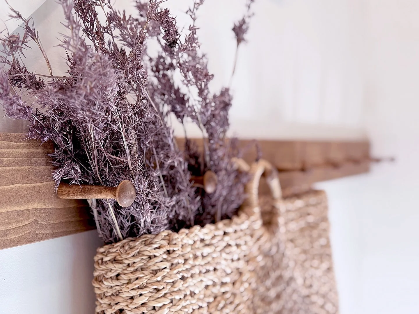 Close-up of lavender flowers in a woven basket hanging on a wooden wall, with a white background.