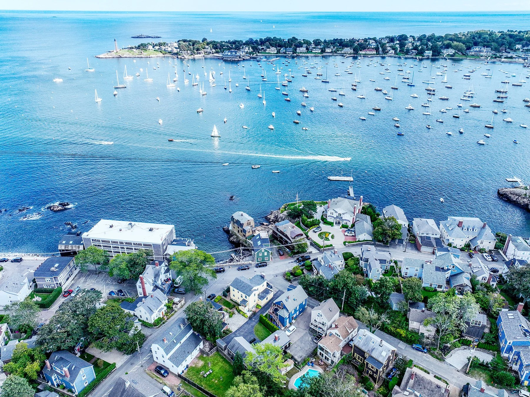 Aerial view of a coastal neighborhood with houses, trees, and a marina filled with sailboats and other boats on the water