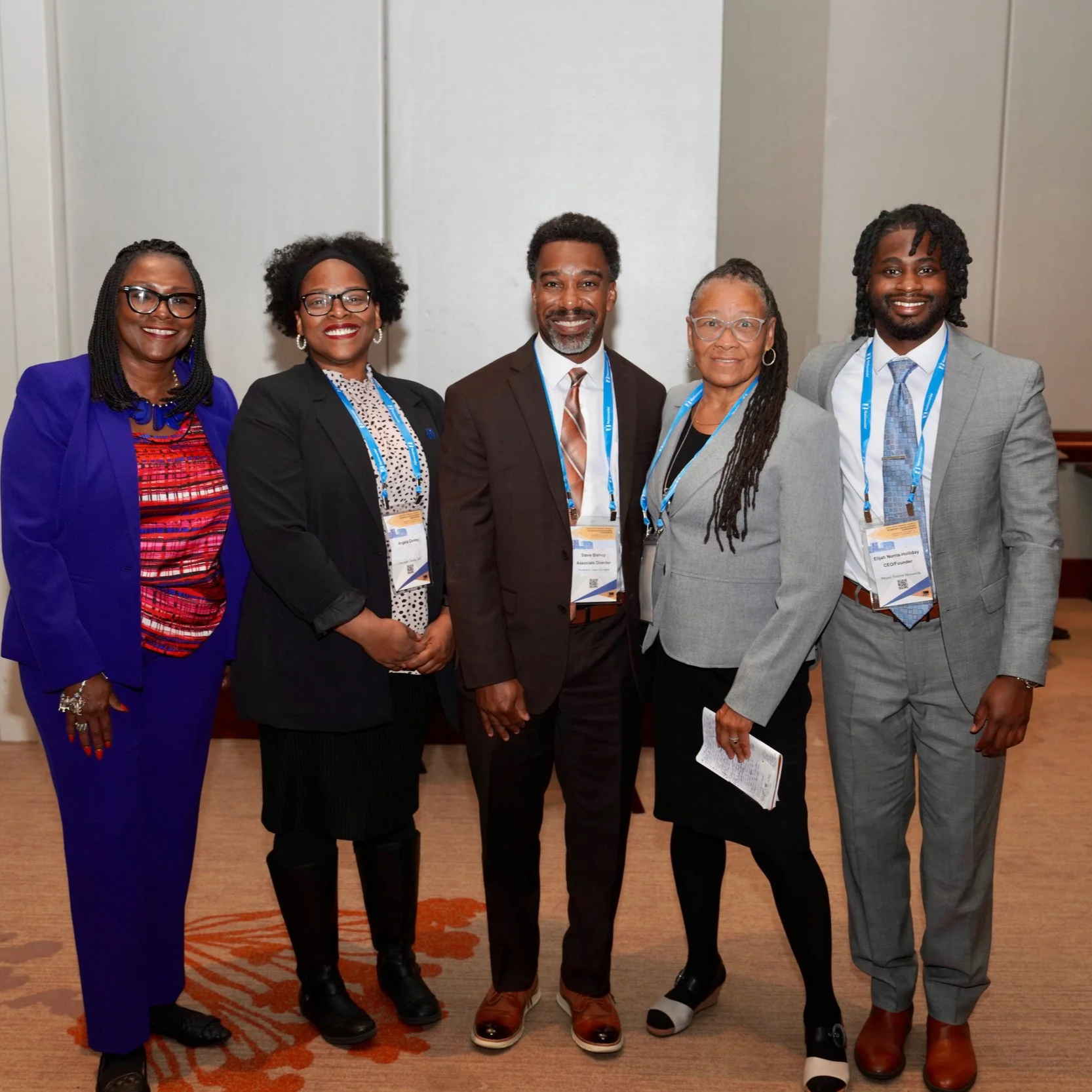 Six professionally dressed individuals standing side by side in a conference room, smiling at the camera.