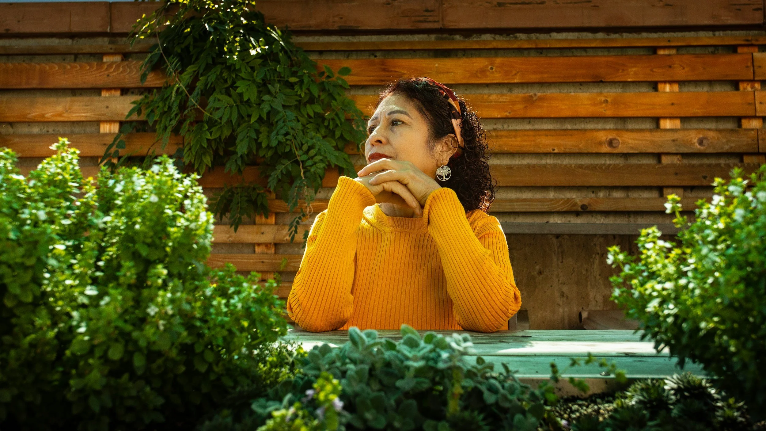 Woman sitting at table looking up with wonder with hands crossed under chin