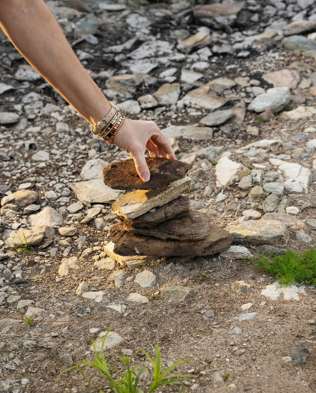 A person arranging rocks in a balanced stack outdoors on rocky ground.