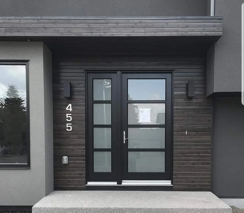 Modern entrance with black double door, side number 455, wall-mounted lights, and a piece of paper on the door.