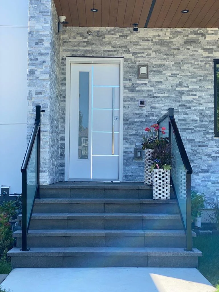 Front entry steps with plants, modern white door with vertical handle, stone exterior wall, and black railing.