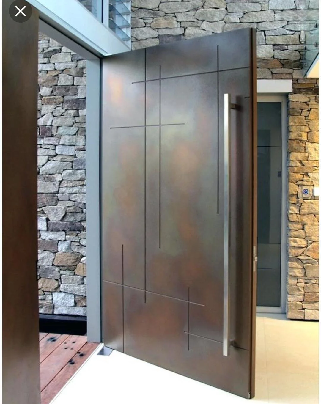 Modern interior door with sleek metal surface and minimalist design, set against a stone wall background.