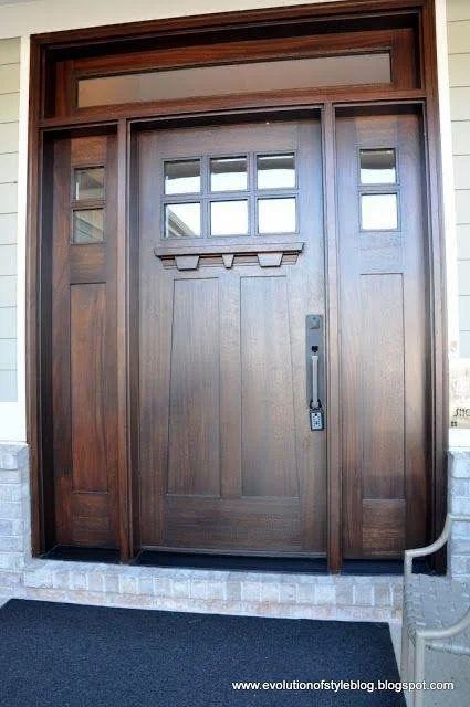 Wooden front door with small window panes, flanked by sidelights with glass, and a transom window above, leading to a brick threshold.