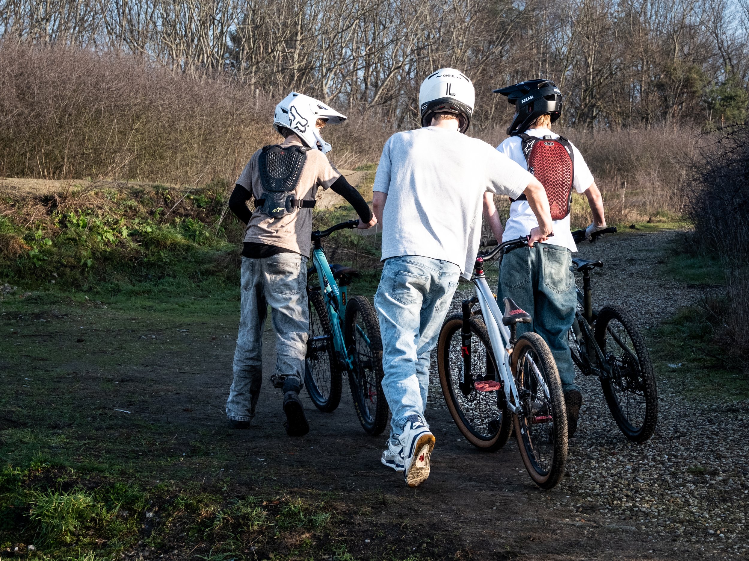 Drie kinderen met fietshelmen en rugzakken, met hun mountainbikes onderweg op een bosachtige trail.