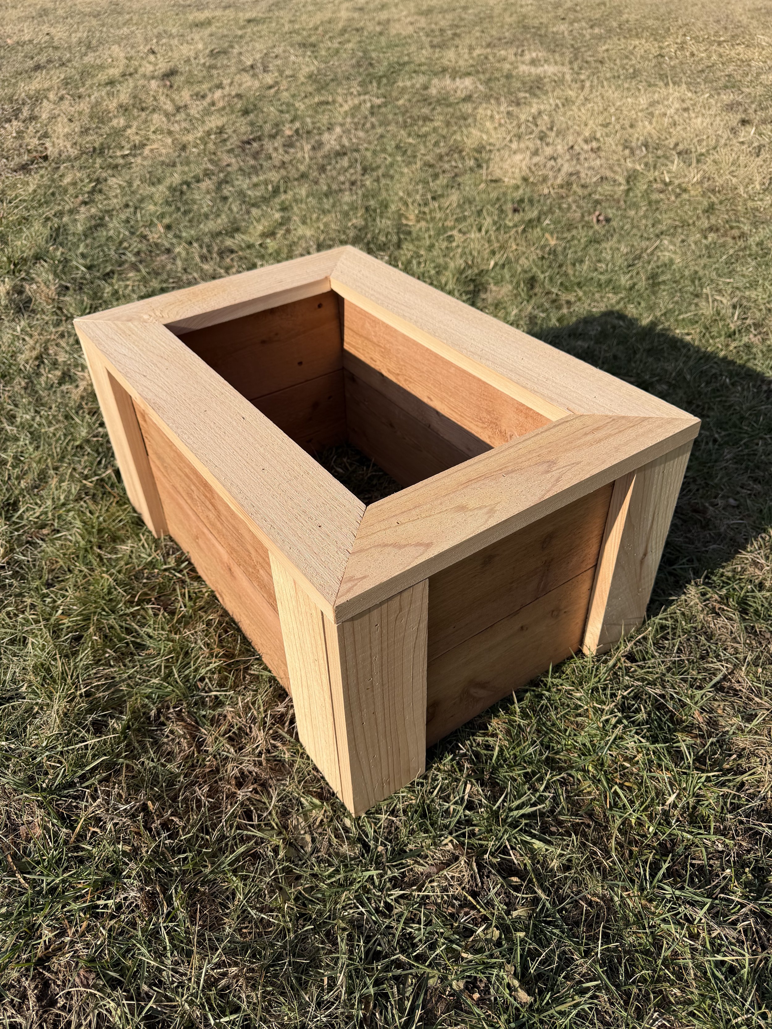 Empty wooden planter box sitting on grass outside.