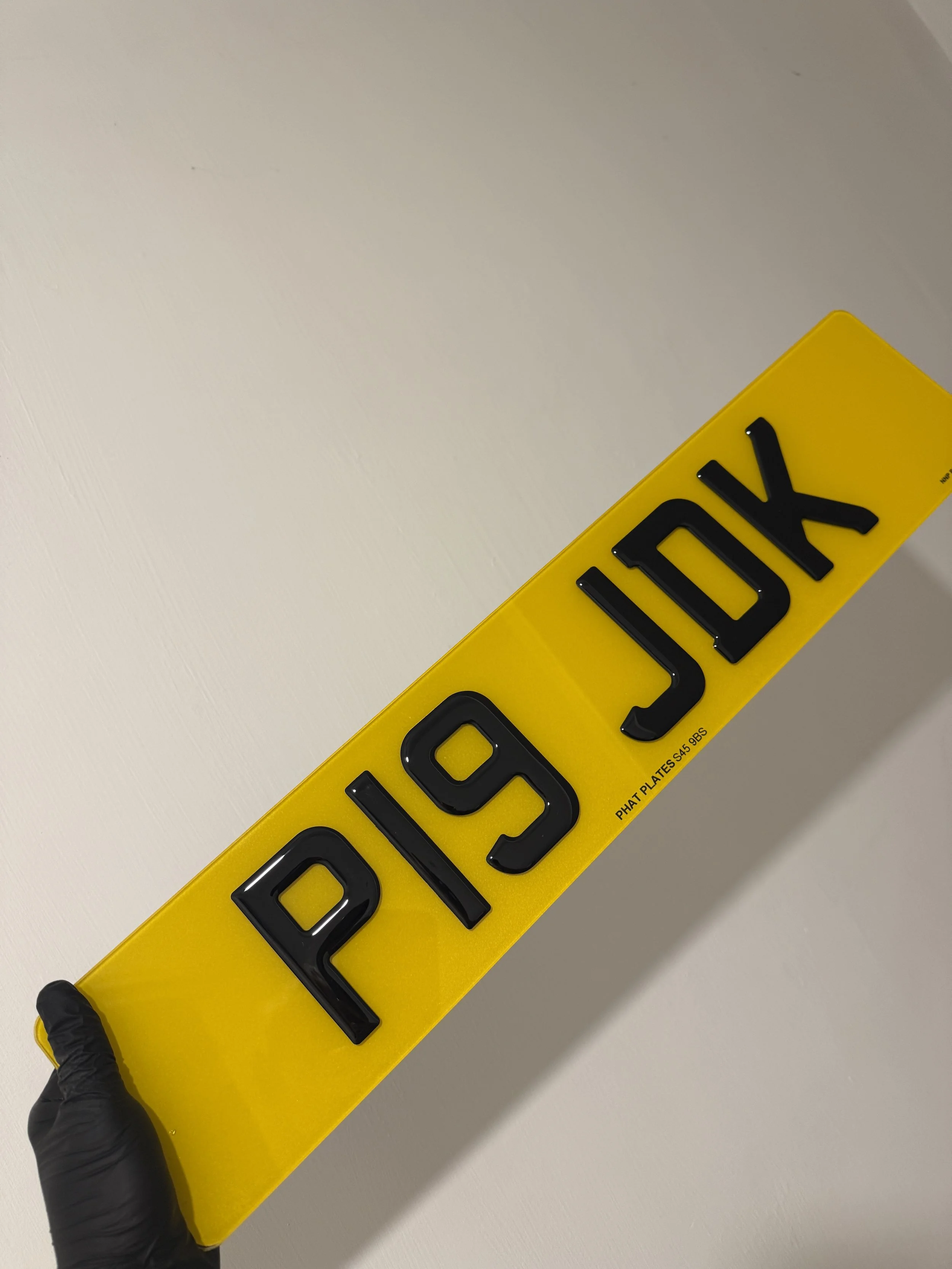 A yellow license plate with black raised letters reading 'PRIDJX' is being held by a person wearing a black glove.