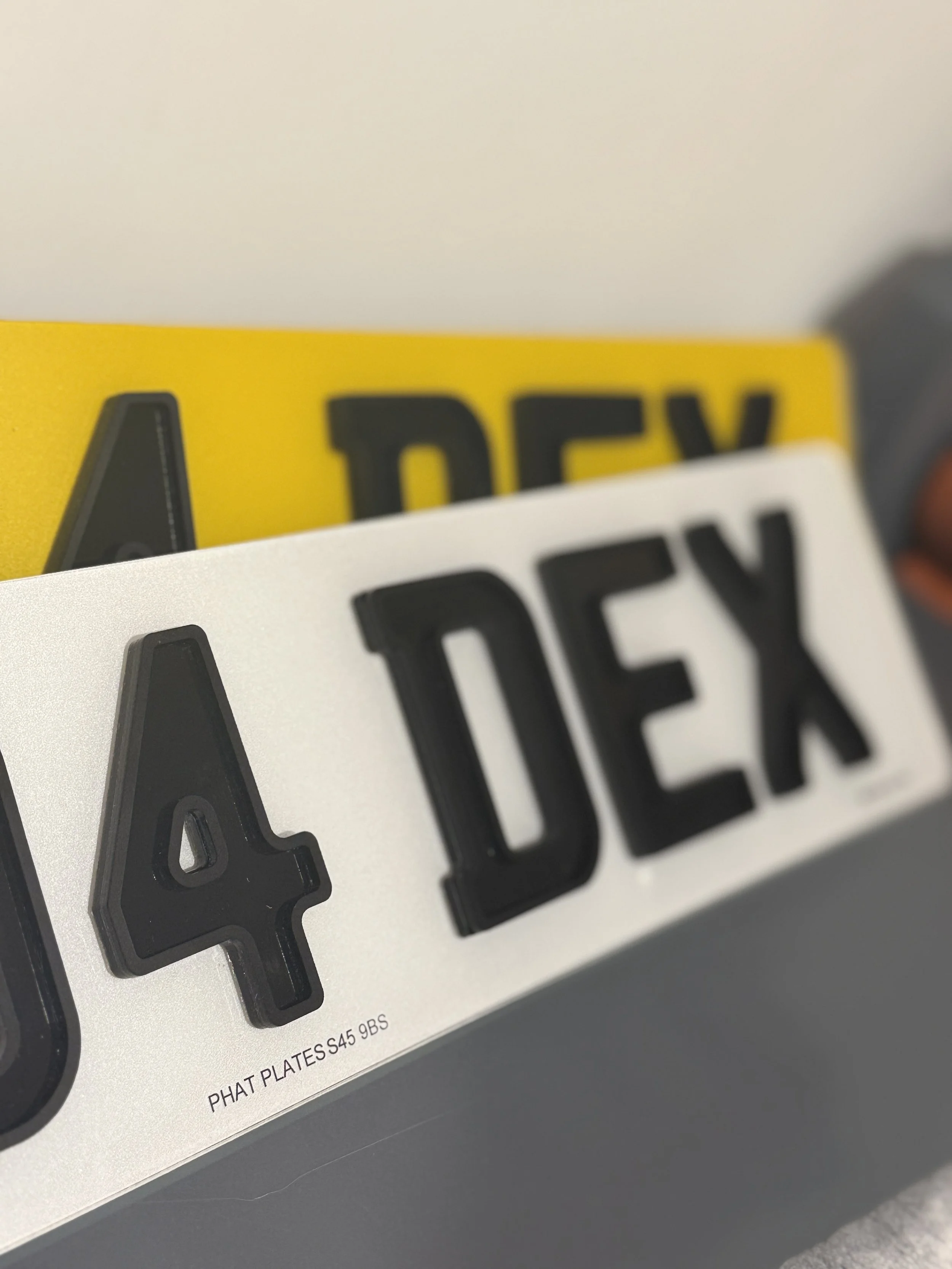 Close-up of a European-style car license plate with the number 40 DEX, with a yellow license plate behind it that has the same number.