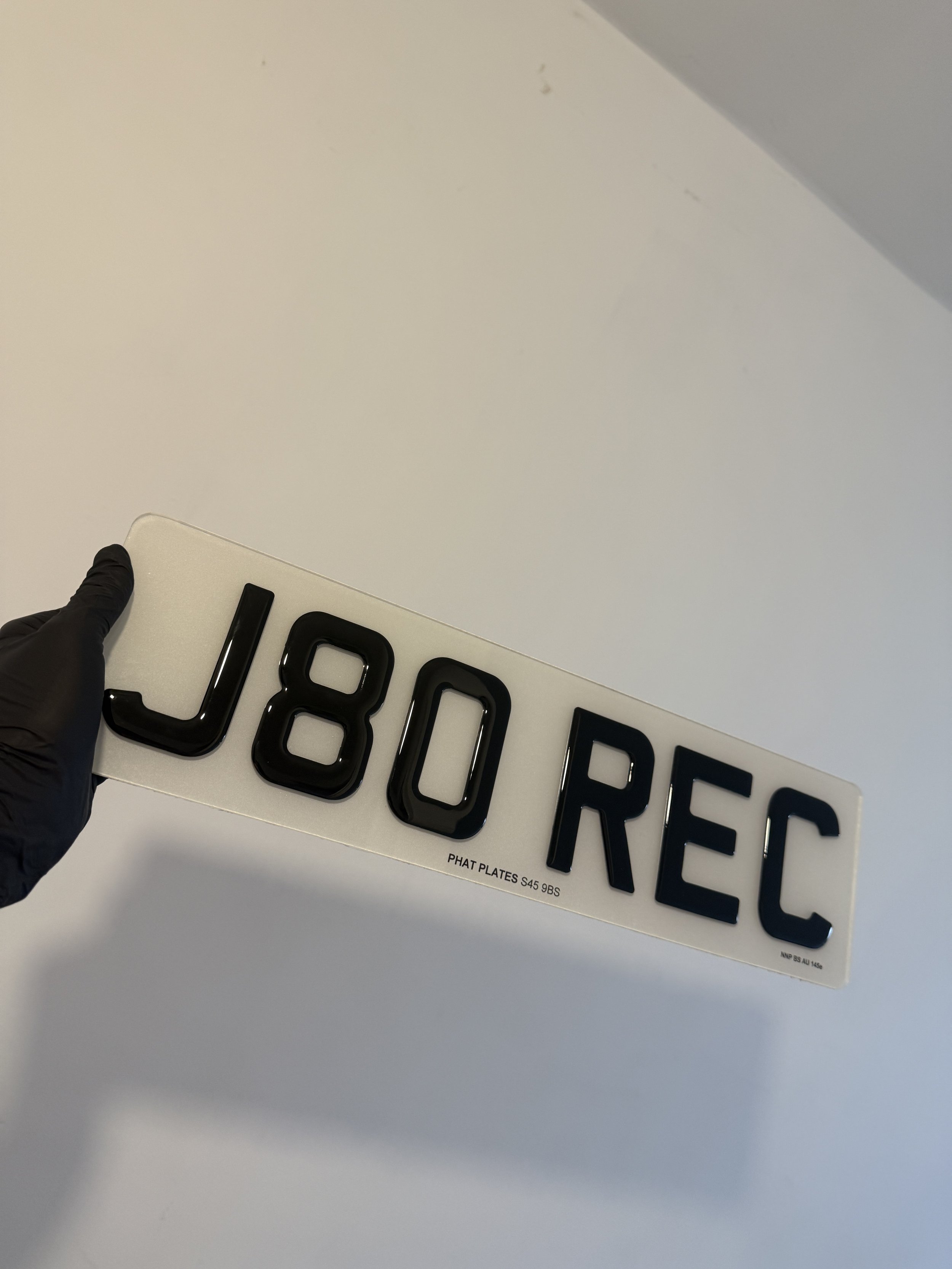 Car license plate with black characters spelling JBO REC held by a person wearing a black glove.