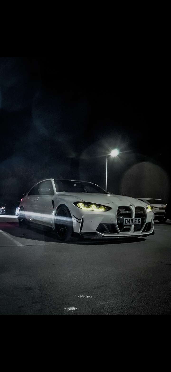 A white sports car parked in a parking lot at night, illuminated by a streetlamp.