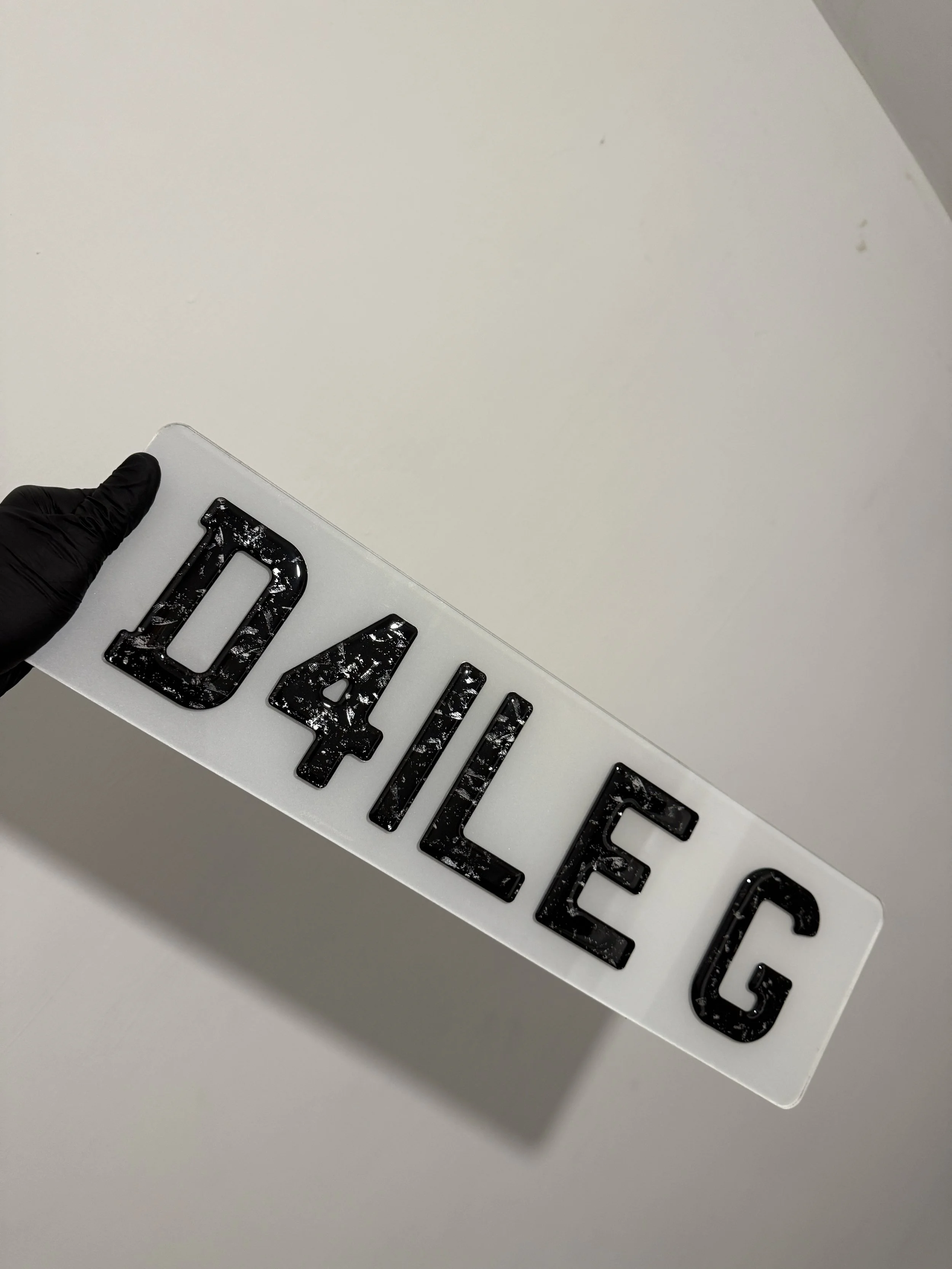 A person wearing black gloves holding a white sign with the word 'DANGLE' in black, marbled letters.