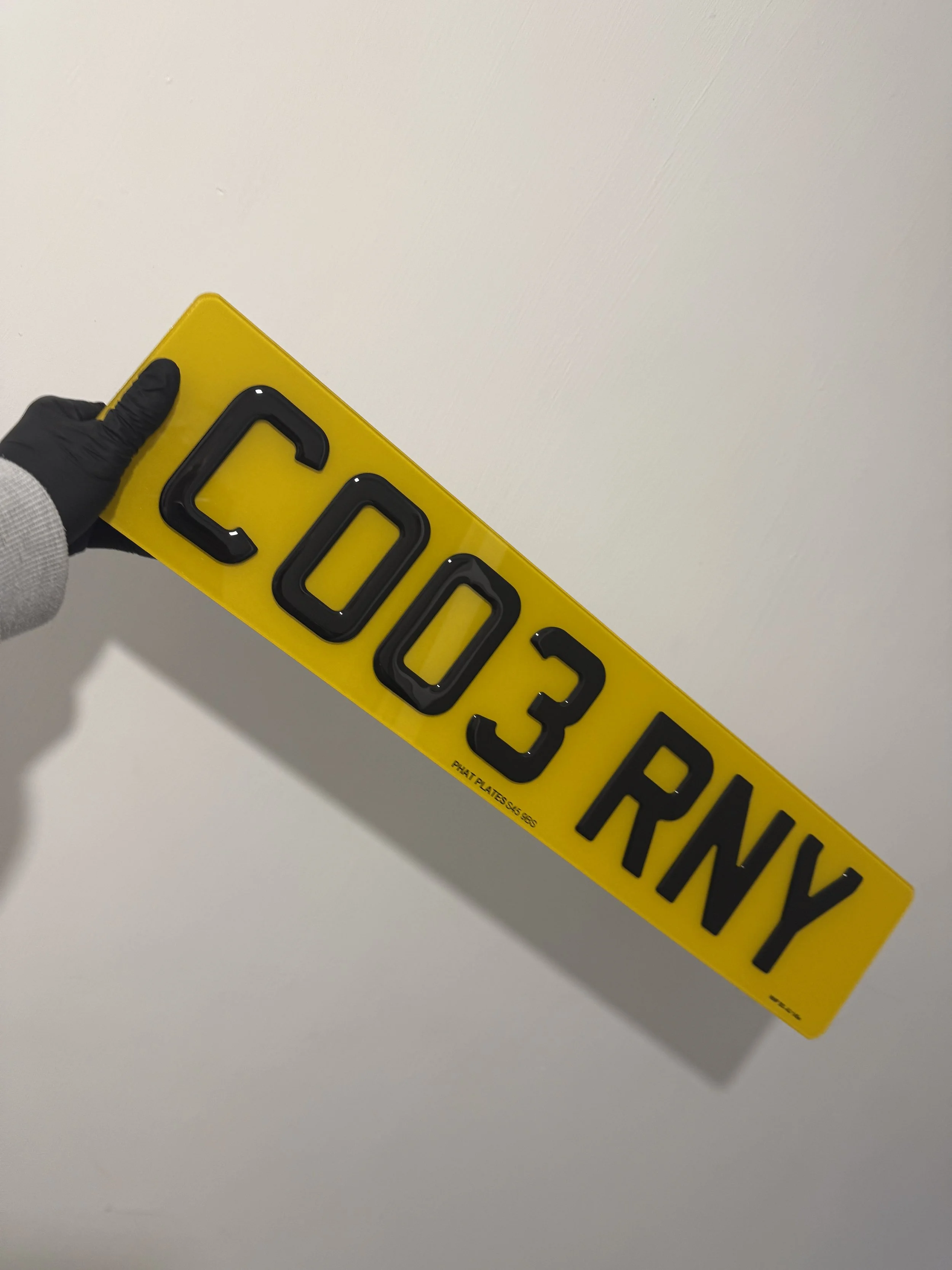 Yellow license plate with the number 003 RNY displayed, held by a person wearing a black glove.
